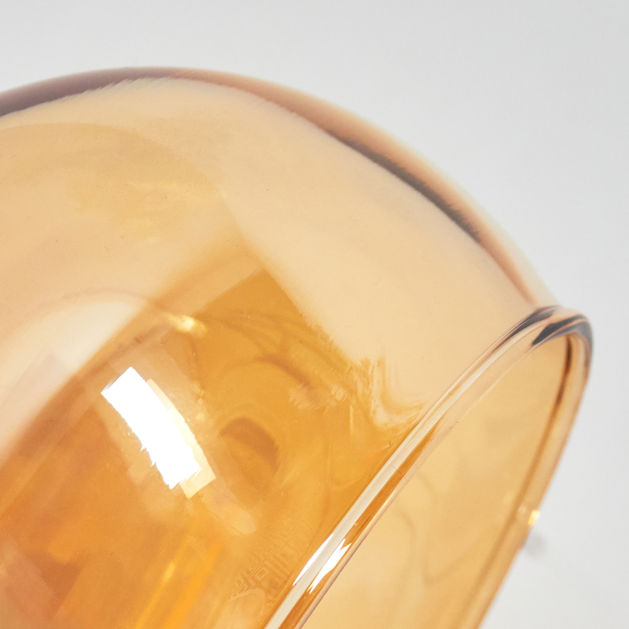 Nahaufnahme einer transparenten, bernsteinfarbenen Glasschale. Der Hintergrund ist weiß.