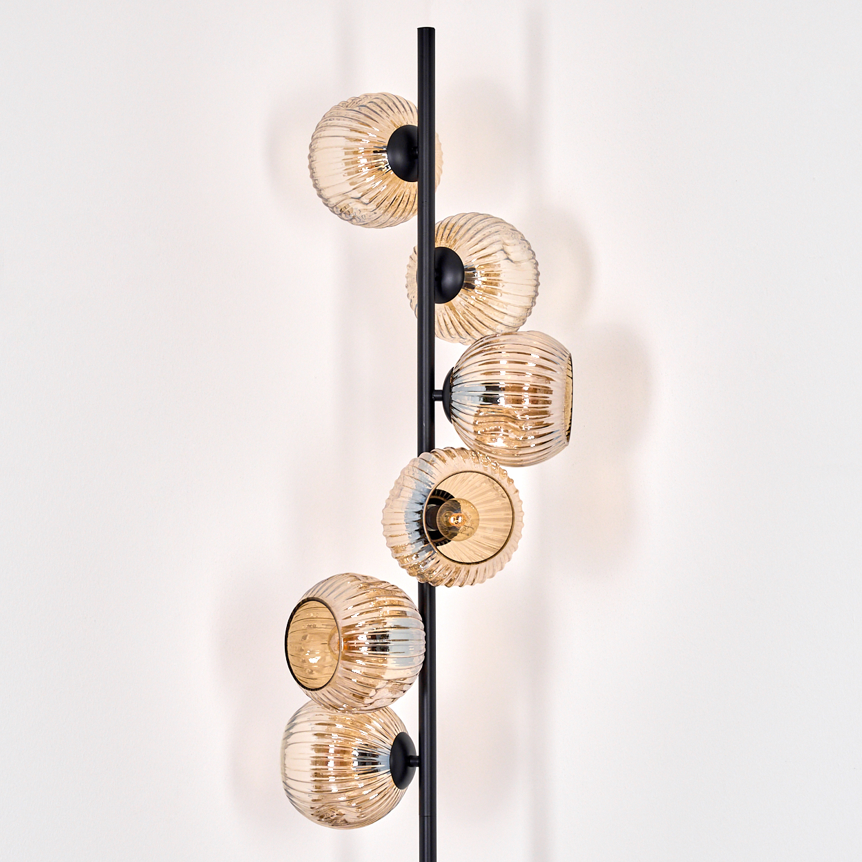 Eine moderne Lampe mit sechs bernsteinfarbenen Glaskugeln an einem schwarzen Pfosten vor einer weißen Wand.