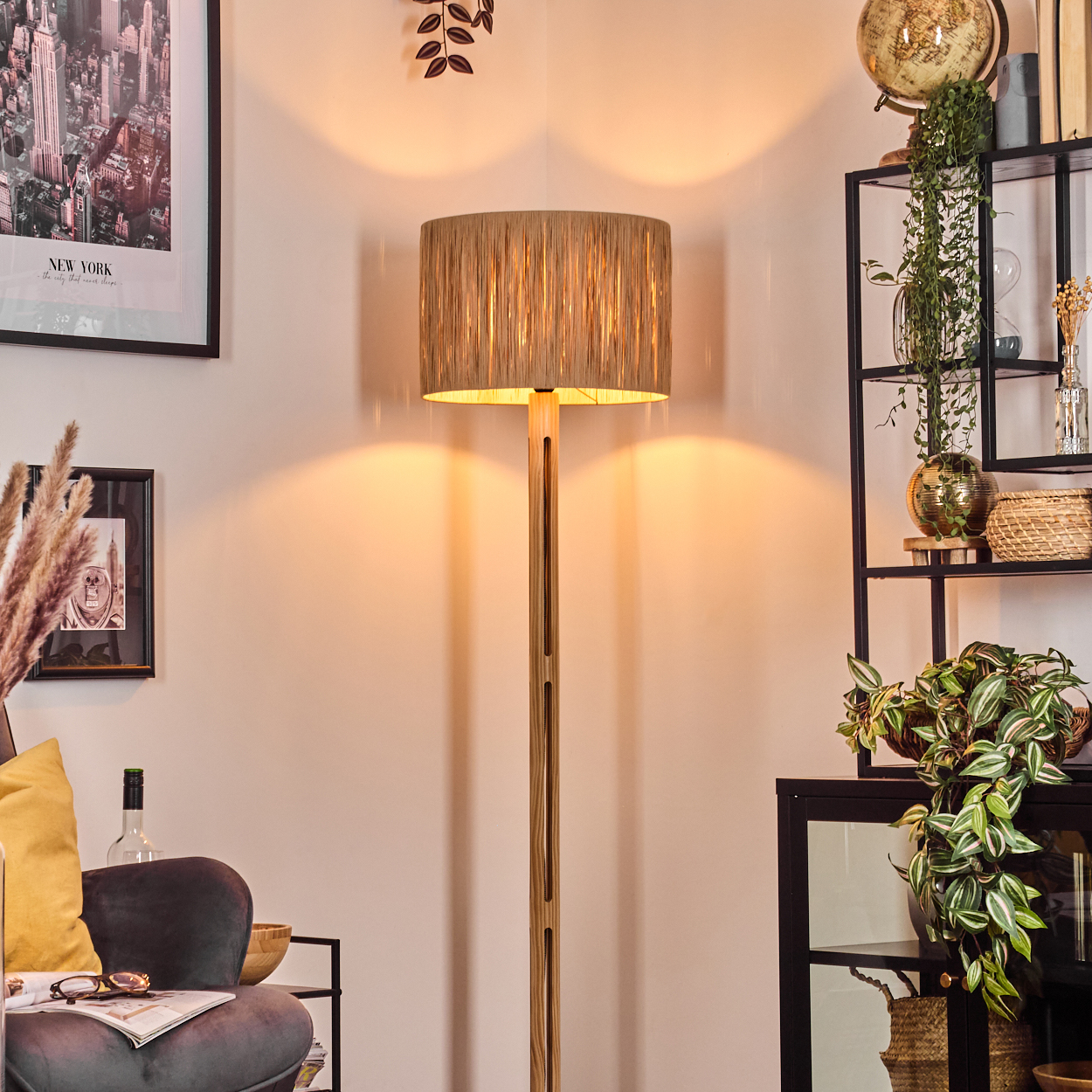 Eine Stehlampe steht in einem Raum mit Regal, Couch und New York-Bild. Pflanzen und Dekoration sind sichtbar.