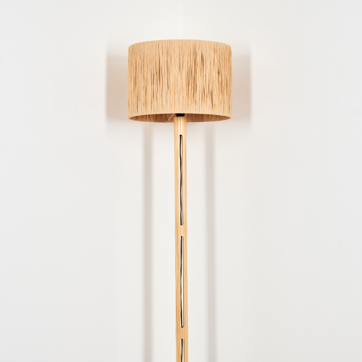 Ein beiger Lampenschirm sitzt auf einer Holzlampe. Die Lampe steht vor einer weißen Wand. Der Lampenschirm hat eine fransenartige Textur.