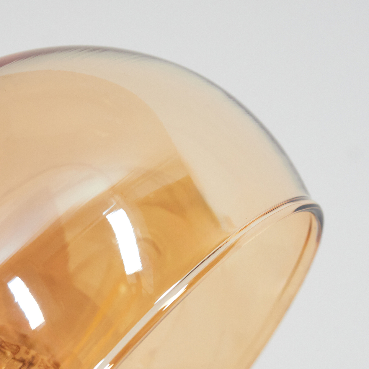 Nahaufnahme eines Glasobjekts. Das Glas ist bernsteinfarben und reflektiert Licht. Ein weißer Hintergrund ist sichtbar.