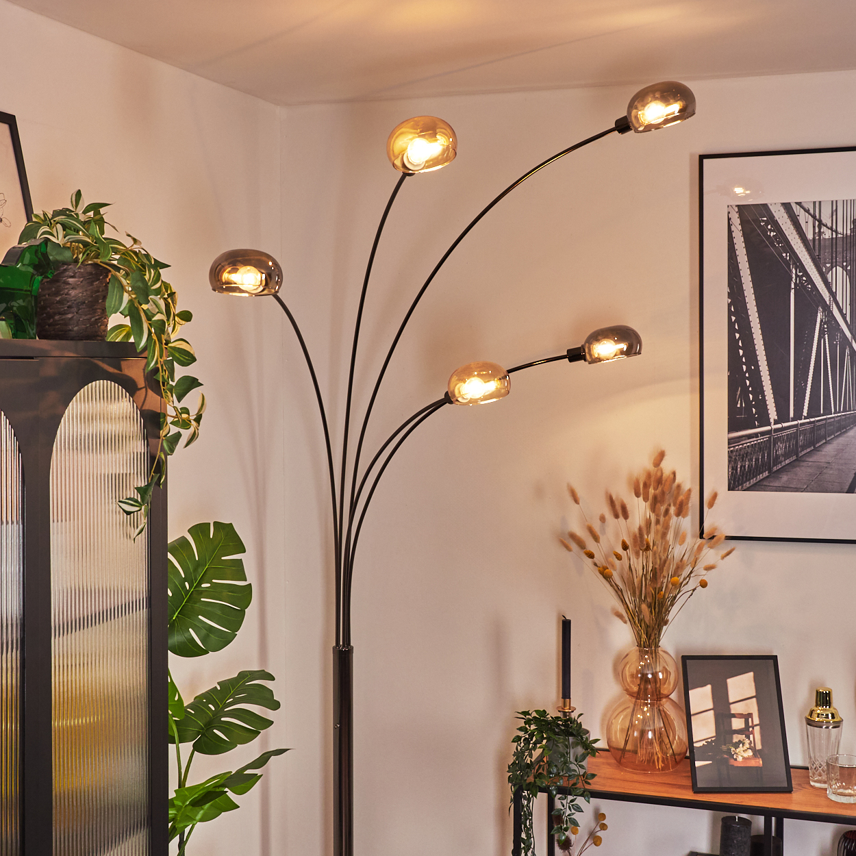 Ein modernes Wohnzimmer mit Stehlampe. Die Lampe hat fünf bernsteinfarbene Glasschirme. Pflanzen und Dekoration sind ebenfalls sichtbar.