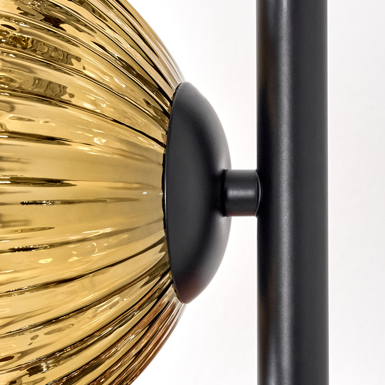 Nahaufnahme einer modernen Lampe. Sie hat einen goldfarbenen, geriffelten Glasschirm und einen schwarzen Metallrahmen. Der Hintergrund ist weiß.