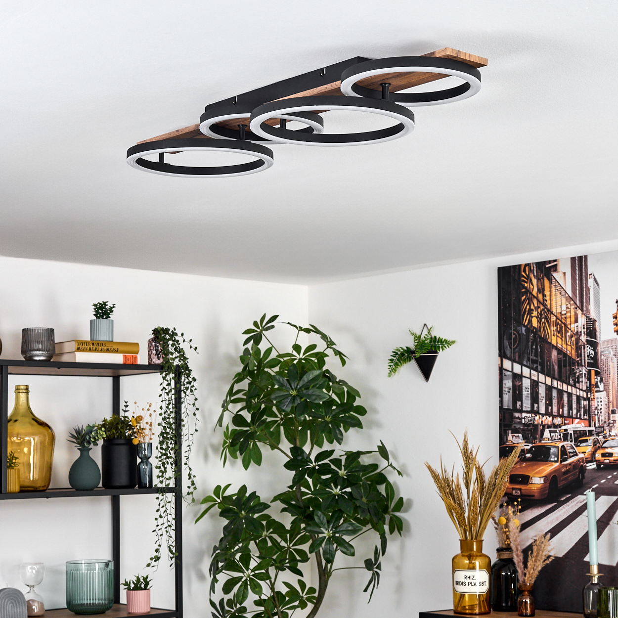 Eine moderne Deckenleuchte mit kreisförmigen Lichtern, Pflanzen, Regalen mit Dekor und einem Gemälde einer New Yorker Straßenszene an der Wand.