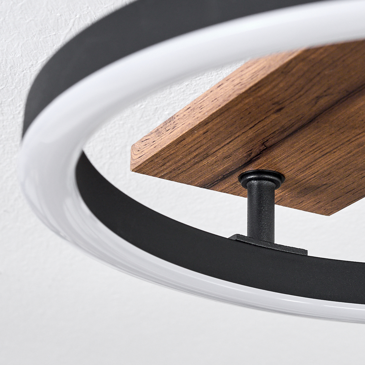 Nahaufnahme einer modernen Leuchte. Sie hat ein Holzregal und ein schwarz-weißes Ringdesign. Der Hintergrund ist eine weiße Wand.