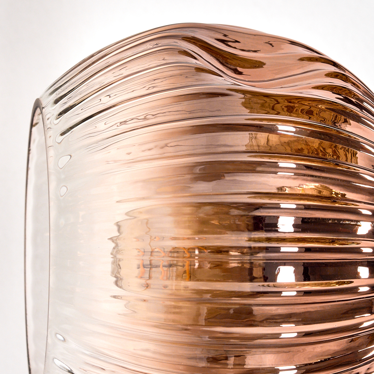 Nahaufnahme eines Glasobjekts mit wellenförmigem, horizontalem Muster. Das Glas hat einen Kupfer- und Klarfarbverlauf, der Licht reflektiert.