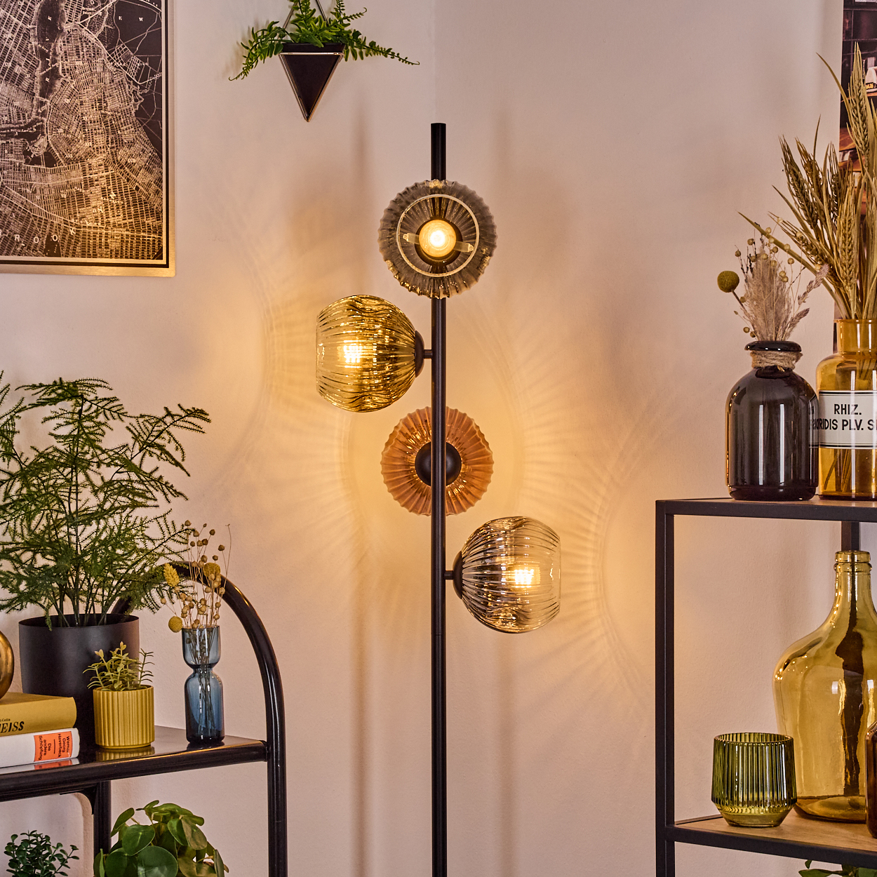 Eine moderne Stehlampe mit drei Glasschirmen. Der Raum hat Regale mit Pflanzen und Vasen. Eine Karte hängt an der Wand.