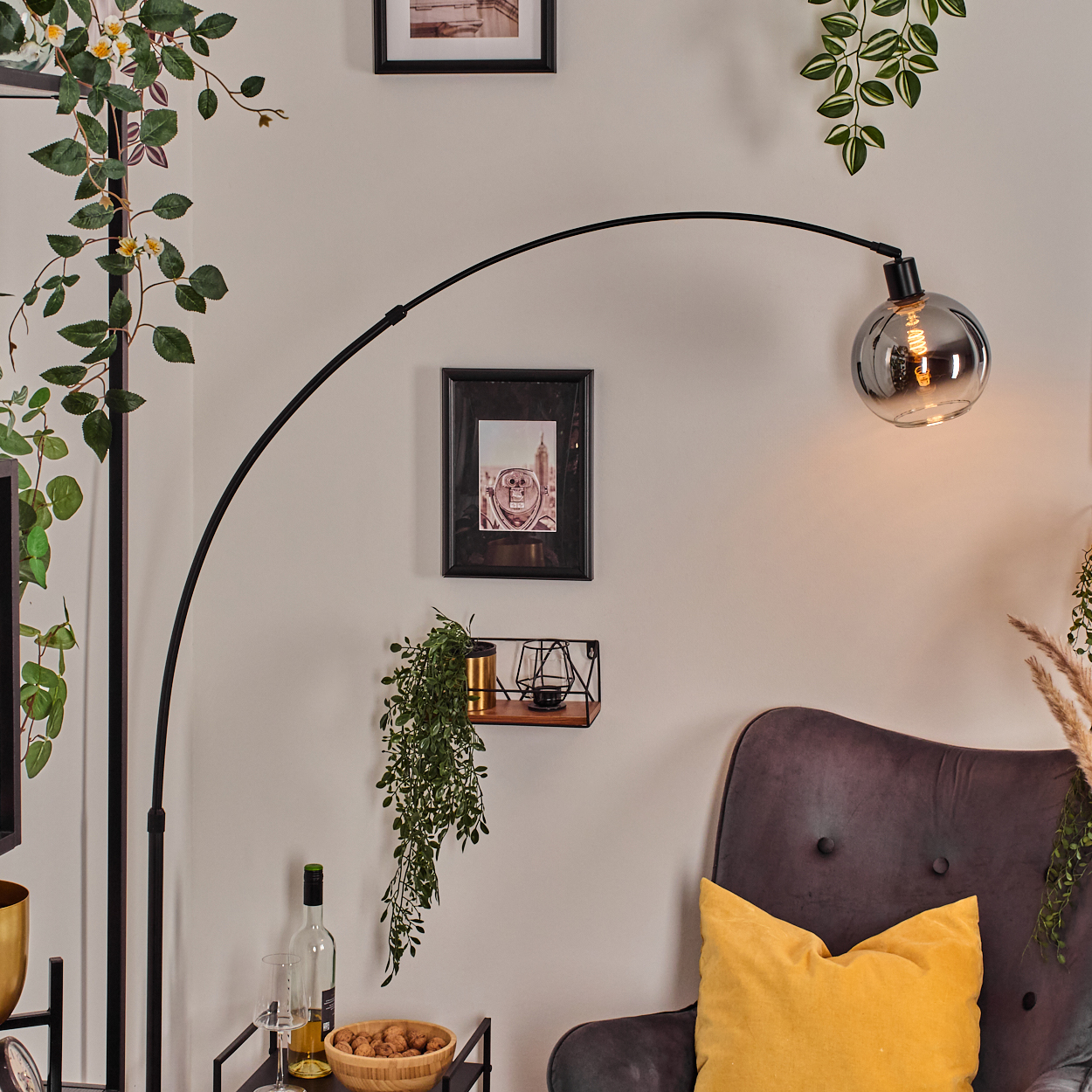 Ein Raum mit Stehlampe, Kunst, Stuhl und Pflanzen. Ein gelbes Kissen auf dem Stuhl, eine Schüssel mit Nüssen und Wein.