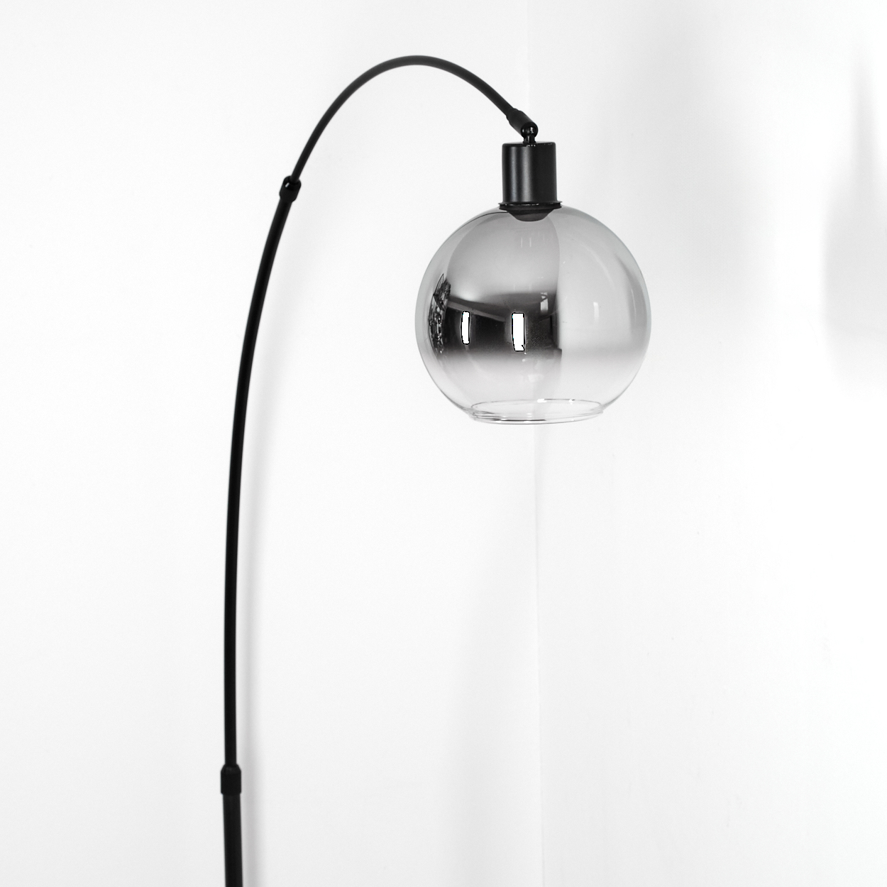 Eine moderne schwarze Bogenlampe mit einem kugelförmigen, rauchigen Glasschirm. Sie steht vor einer weißen Eckwand.