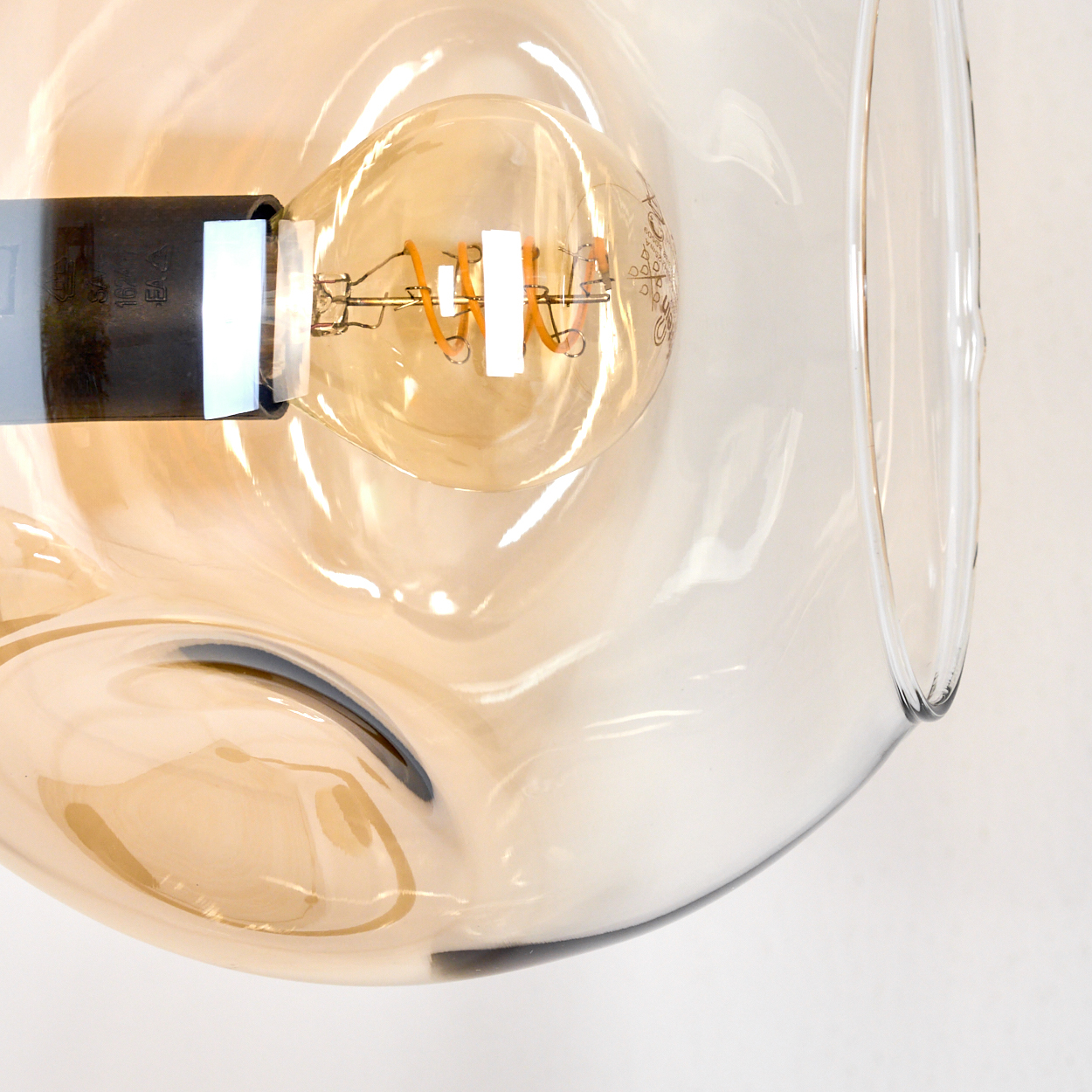 Nahaufnahme einer Glühbirne in einem durchsichtigen Glasschirm. Die Glühbirne hat einen Spiralfaden und der Schirm ein wellenförmiges Design.