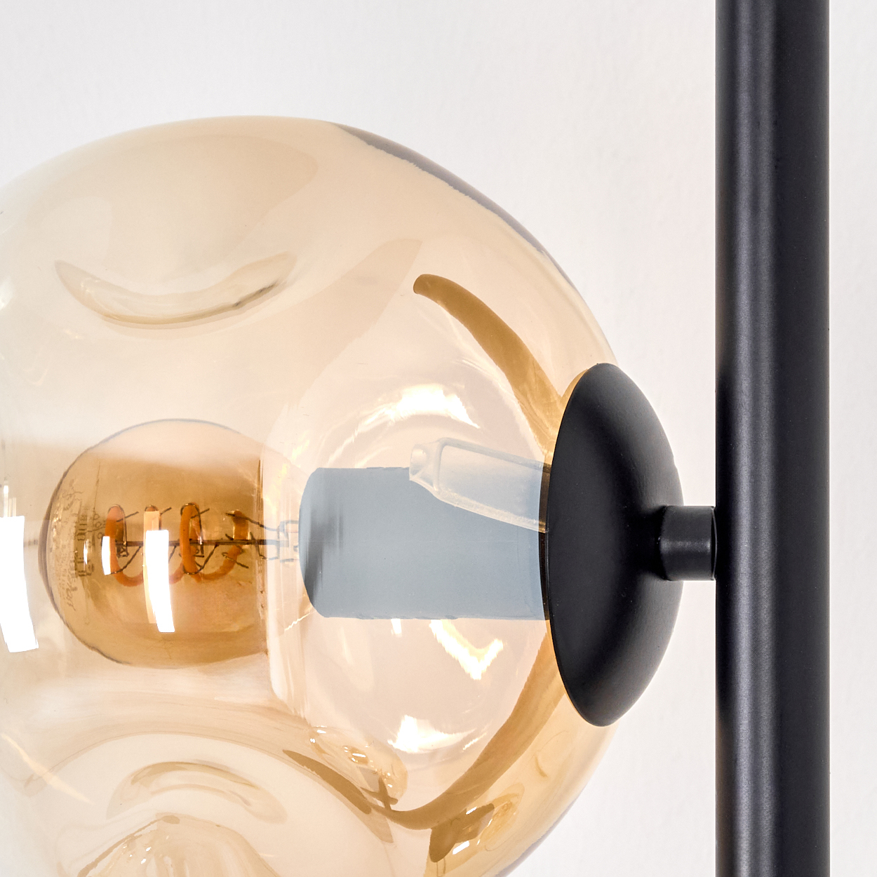 Nahaufnahme einer modernen Lampe. Sie hat einen runden, bernsteinfarbenen Glasschirm mit einer sichtbaren Glühbirne.