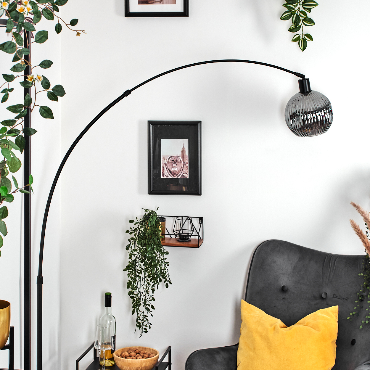 Eine Zimmerecke mit Stehlampe, Kunst, Regal mit Pflanzen, Stuhl mit gelbem Kissen und Tisch mit Snacks.