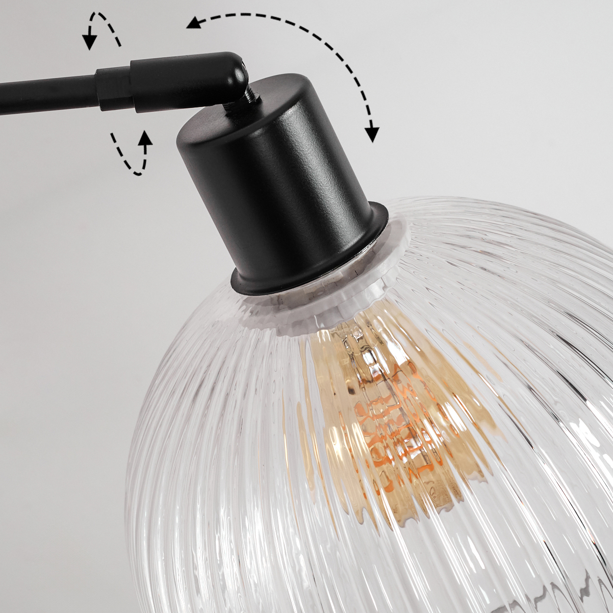 Nahaufnahme einer schwarzen Lampe mit klarem, geripptem Glasschirm. Die Glühbirne leuchtet. Pfeile zeigen verstellbare Positionen an.