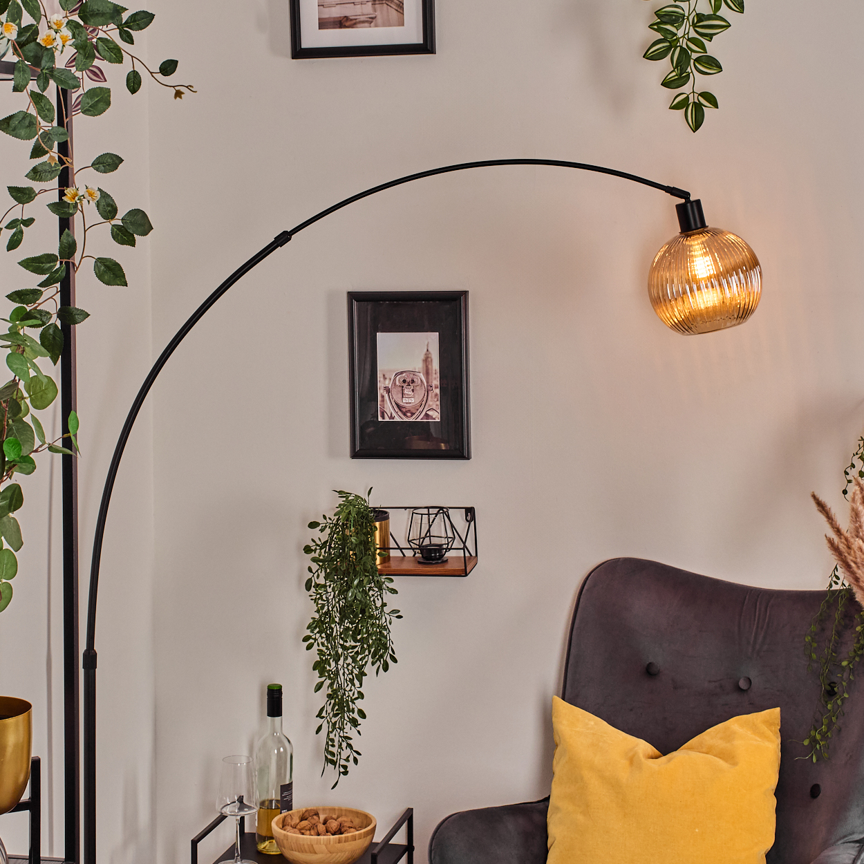 Ein modernes Wohnzimmer mit schwarzer Bogenlampe, grauem Sessel, gelbem Kissen und dekorativen Pflanzen.