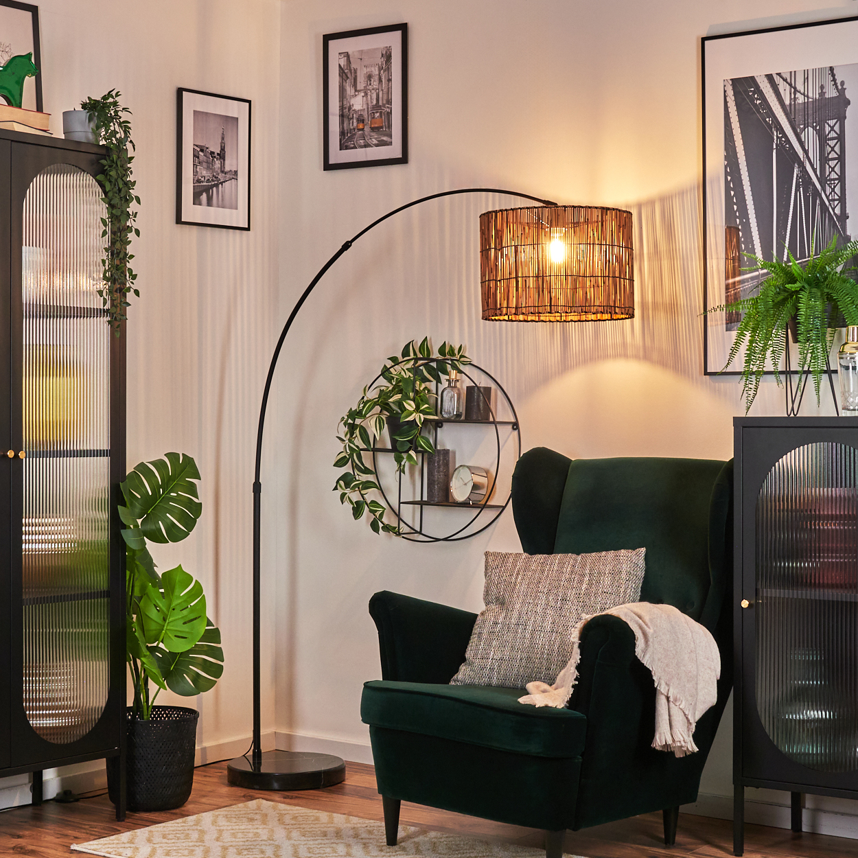 Ein Zimmer mit grünem Sessel, Stehlampe und schwarzem Schrank. Bilder an der Wand und Pflanzen. Warmes, einladendes Interieur.