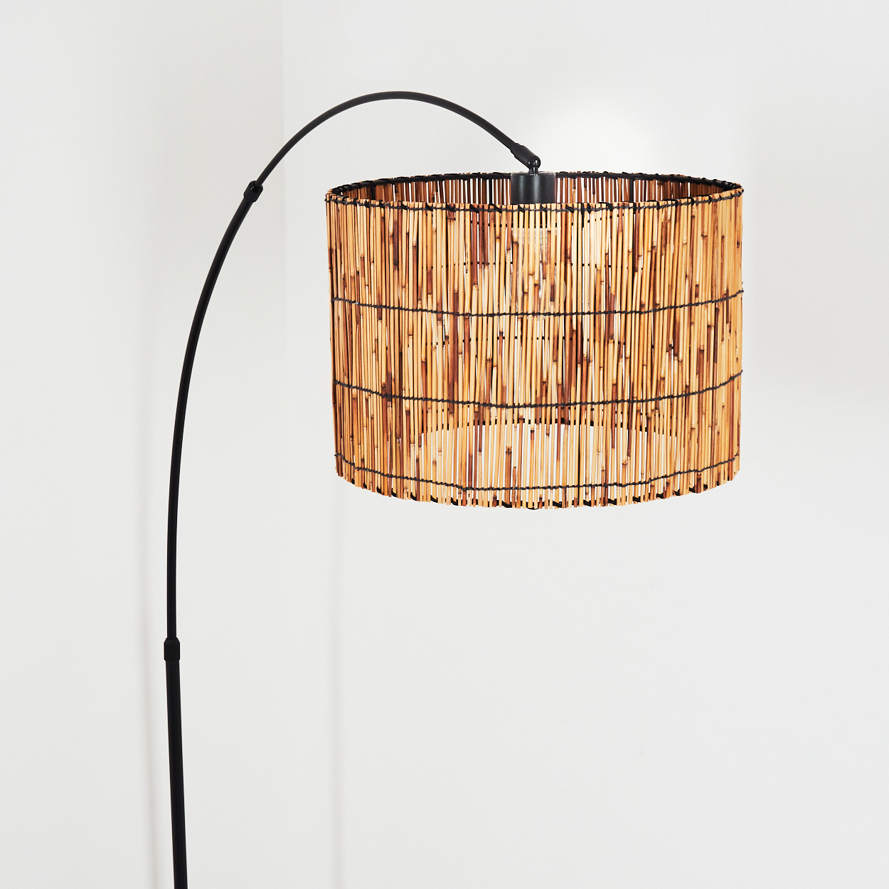 Eine Stehlampe mit Bambusschatten und schwarzem Metallrahmen. Der Hintergrund ist schlicht weiß.