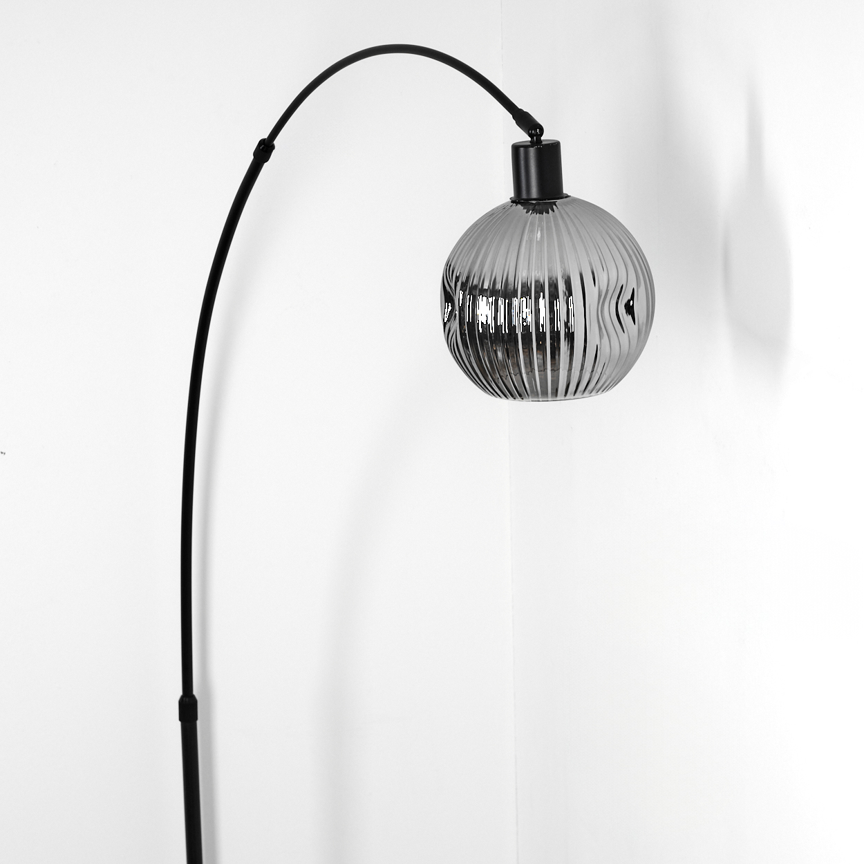 Eine moderne schwarze Stehlampe mit rundem, geripptem, grauem Glasschirm. Sie steht in einer Ecke vor einer weißen Wand.