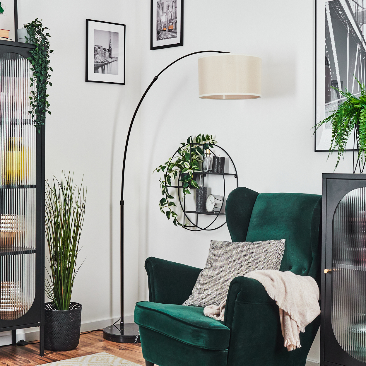 Ein grüner Sessel mit Kissen und Decke, eine schwarze Lampe, eine Pflanze und Bilder an einer weißen Wand.