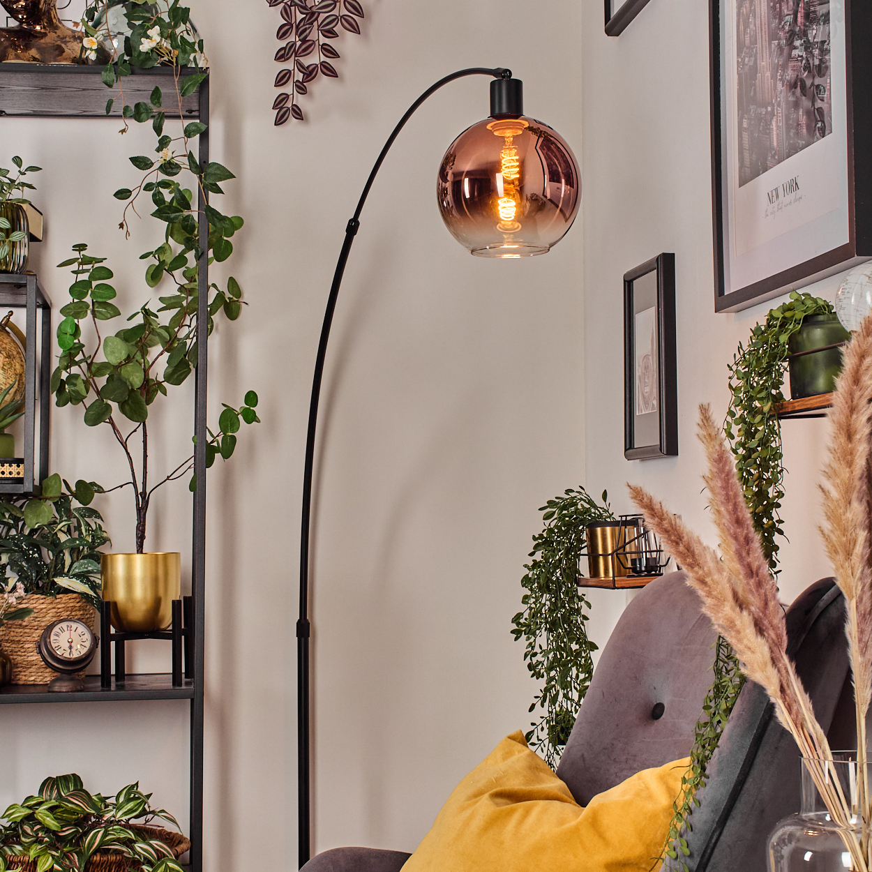Ein modernes Wohnzimmer mit Stehlampe, Pflanzen und einem grauen Sessel mit gelbem Kissen. Ein New York-Poster hängt an der Wand.