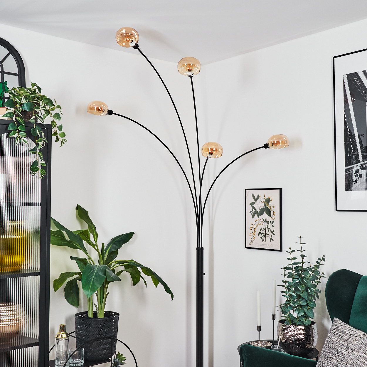 Ein modernes Wohnzimmer mit einer schwarzen Stehlampe mit fünf Kugellampen. Pflanzen, Bilder und ein grüner Sessel sind ebenfalls sichtbar.