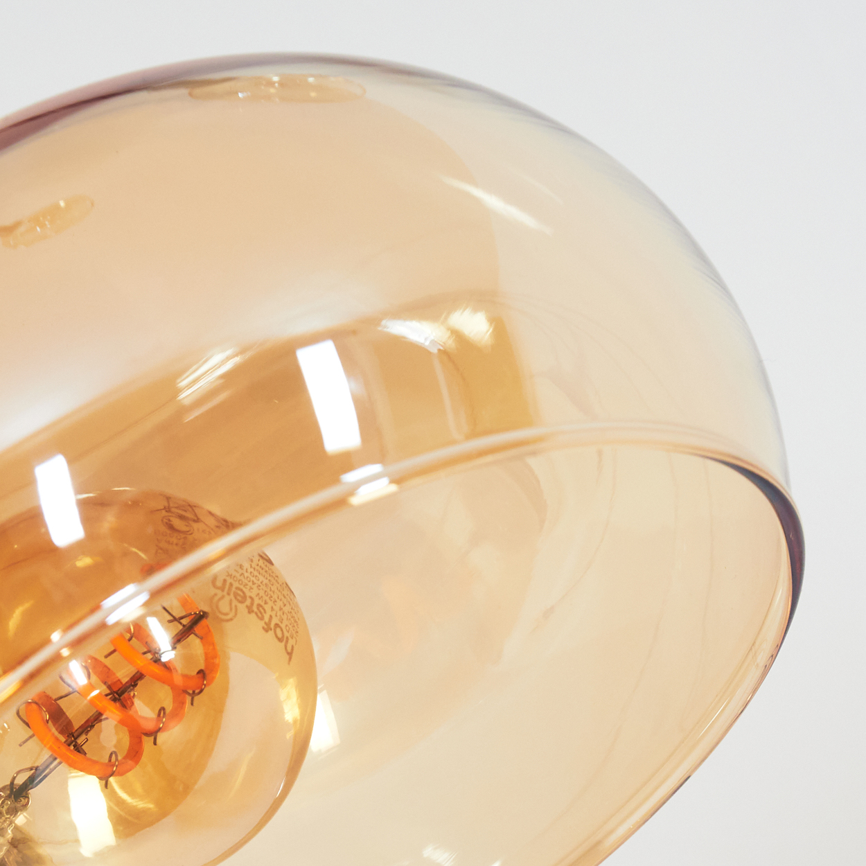 Nahaufnahme einer Glaslampe mit einer warm getönten Glühbirne. Das Glas hat einen Bernsteinton, der Hintergrund ist weiß.