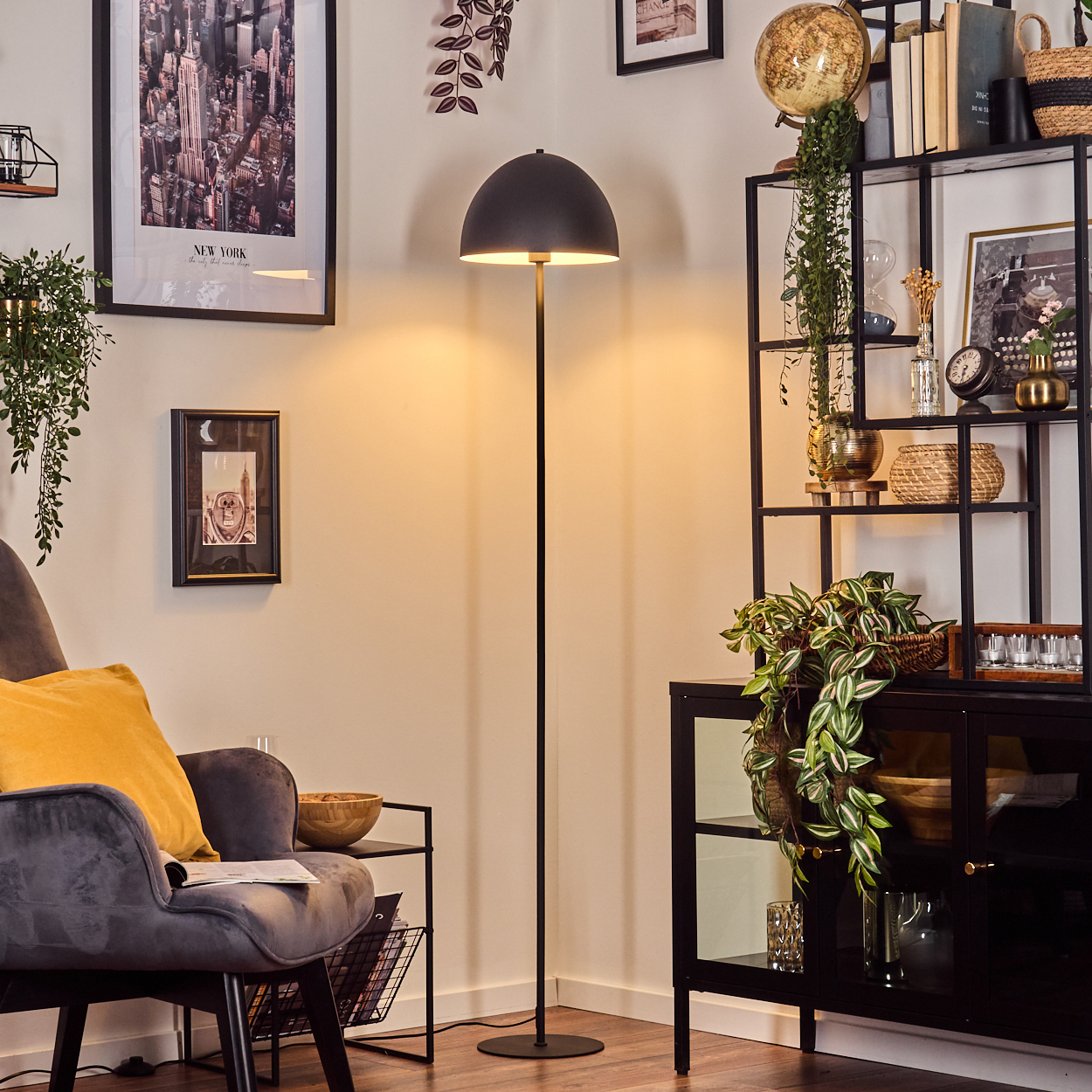 Ein Raum mit einer Stehlampe. Links ein Stuhl mit gelbem Kissen. Regale mit Dekorationen im Hintergrund.