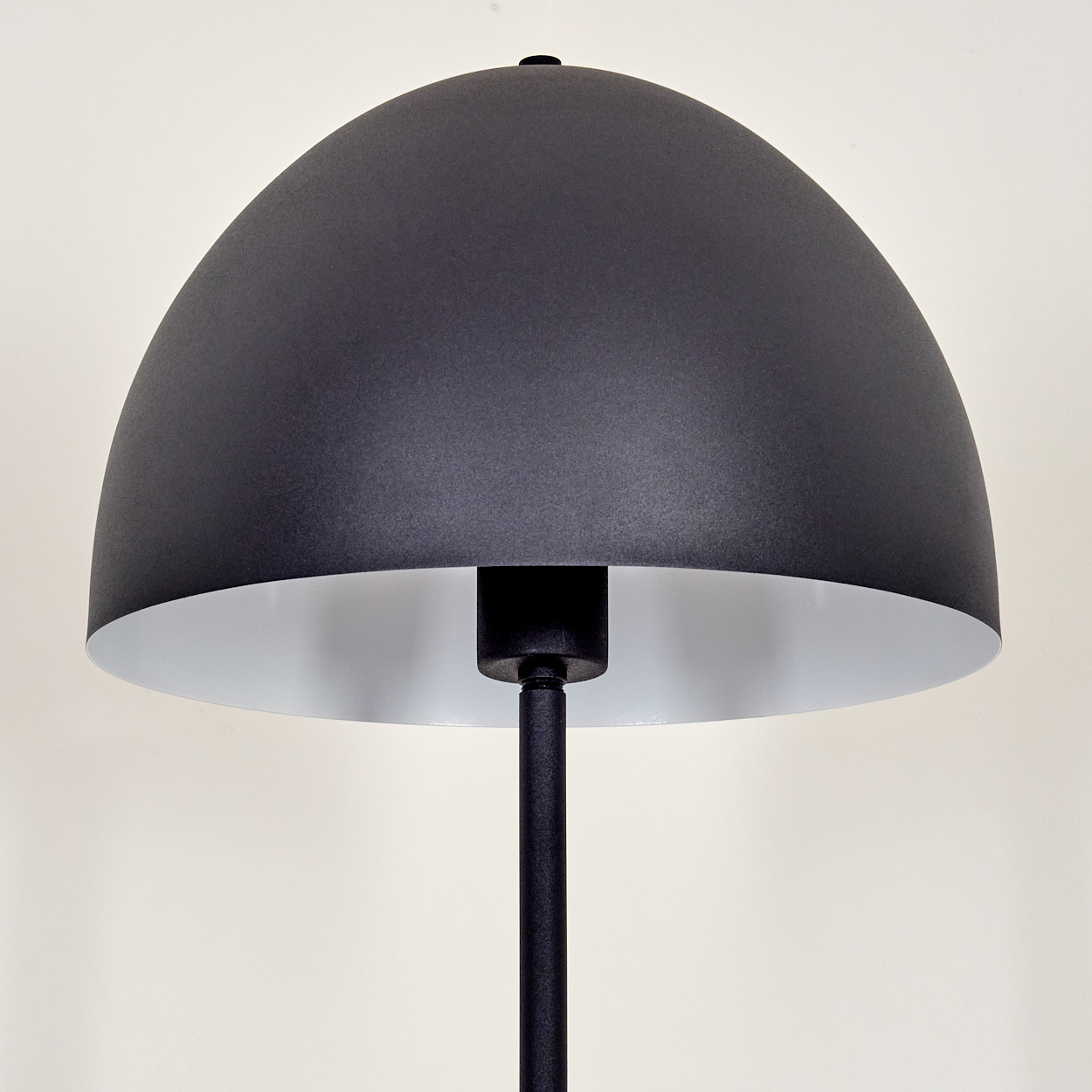 Eine moderne schwarze Lampe mit halbkugelförmigem Schirm und silbernem Innenraum. Sie hat einen schwarzen Stiel auf beigem Hintergrund.