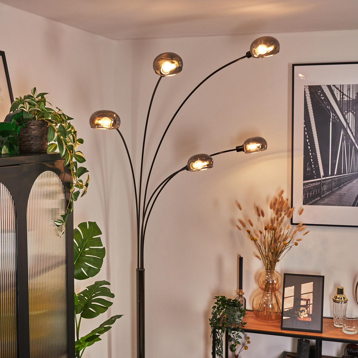 Ein modernes Wohnzimmer mit einer Stehlampe. Die Lampe hat fünf Kugellampen. Pflanzen und Bilder schmücken den Raum.
