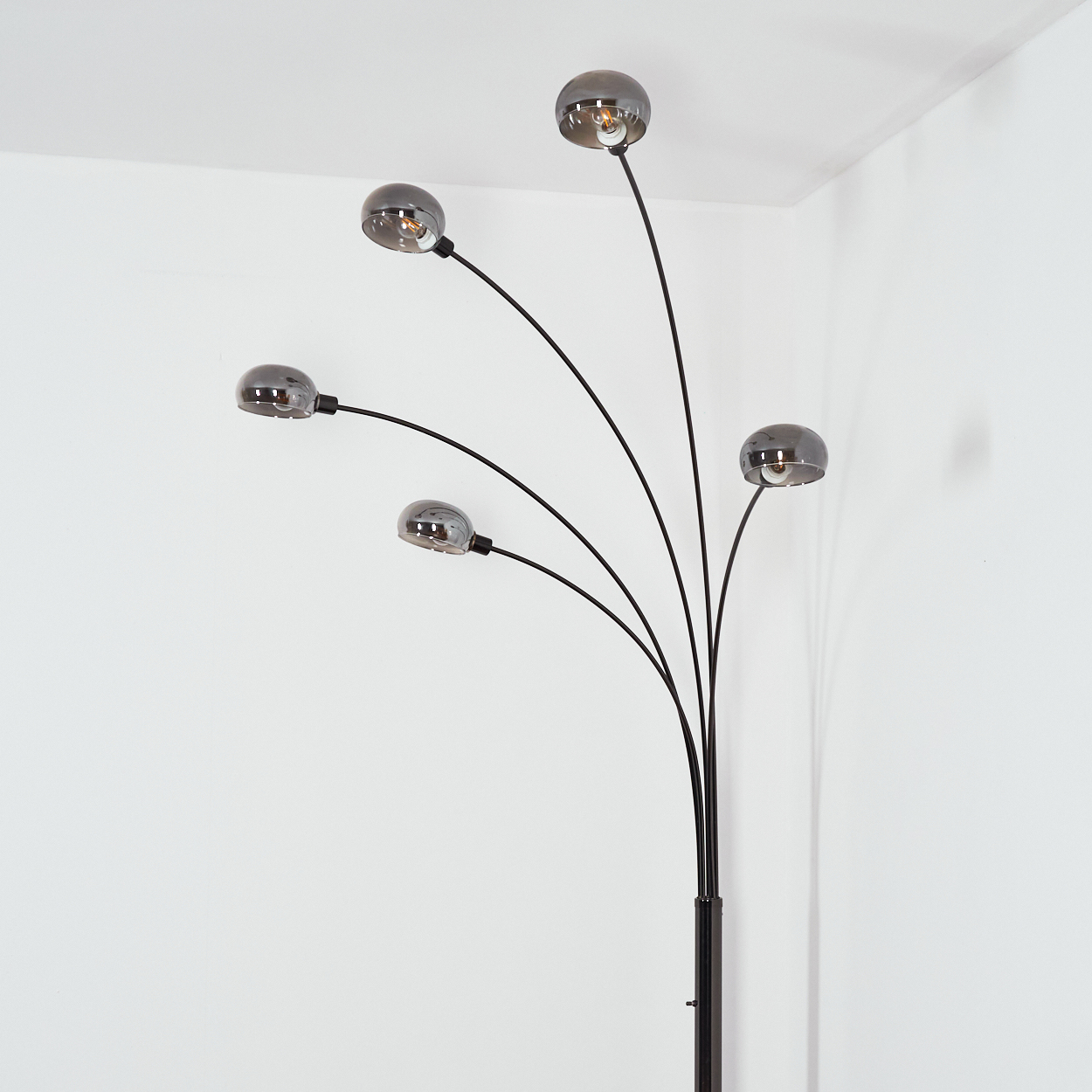 Eine moderne Stehlampe mit fünf gebogenen schwarzen Armen und grauen, kugelförmigen Schirmen vor weißer Wand.