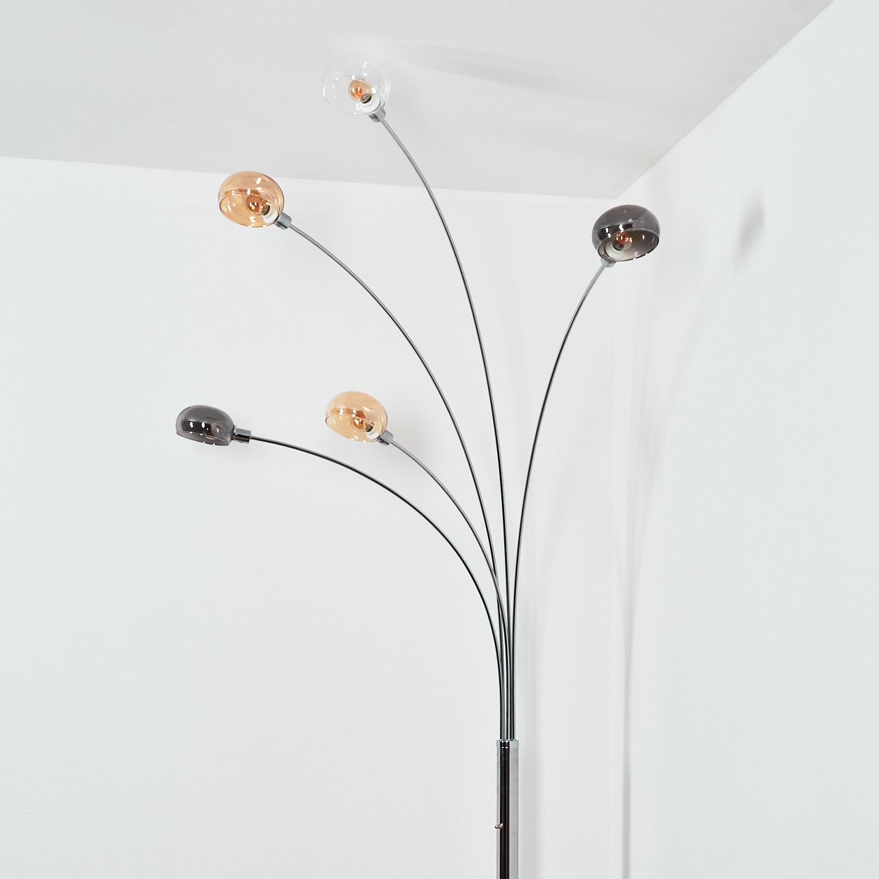 Eine moderne Stehlampe mit fünf gebogenen Armen, die jeweils eine runde, farbige Glühbirne halten. Der Hintergrund ist eine weiße Ecke.