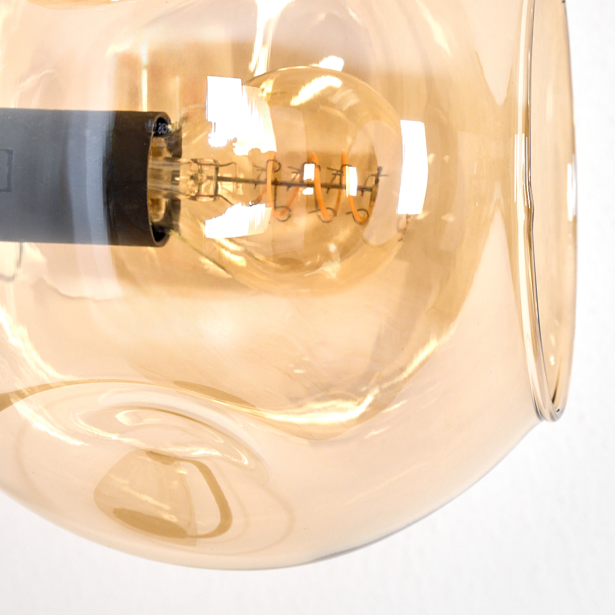 Nahaufnahme einer Glühbirne in einem goldenen Glasschirm. Der Glühfaden der Glühbirne ist sichtbar, das Glas reflektiert Licht.