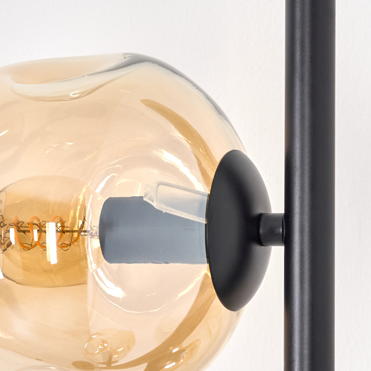 Nahaufnahme einer modernen Lampe. Eine große, bernsteinfarbene Glühbirne ist mit einem schwarzen Metallrahmen verbunden. Weißer Hintergrund.