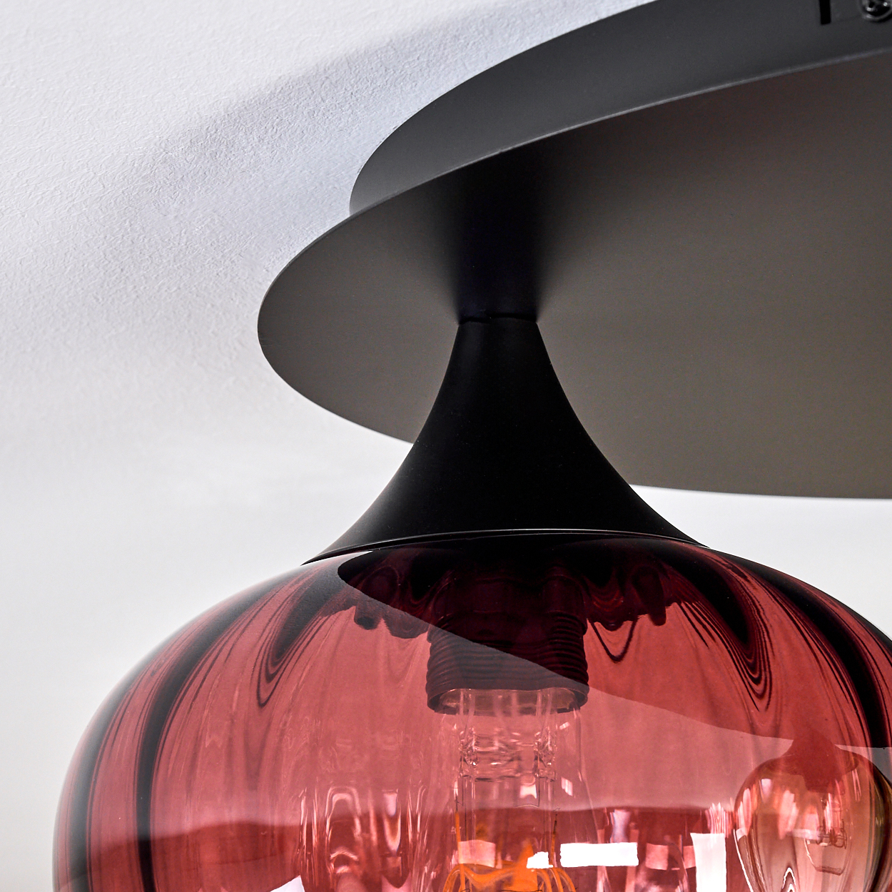 Eine moderne Deckenlampe mit rotem Glasschirm und schwarzem Metallgestell. Die Glühbirne ist sichtbar.