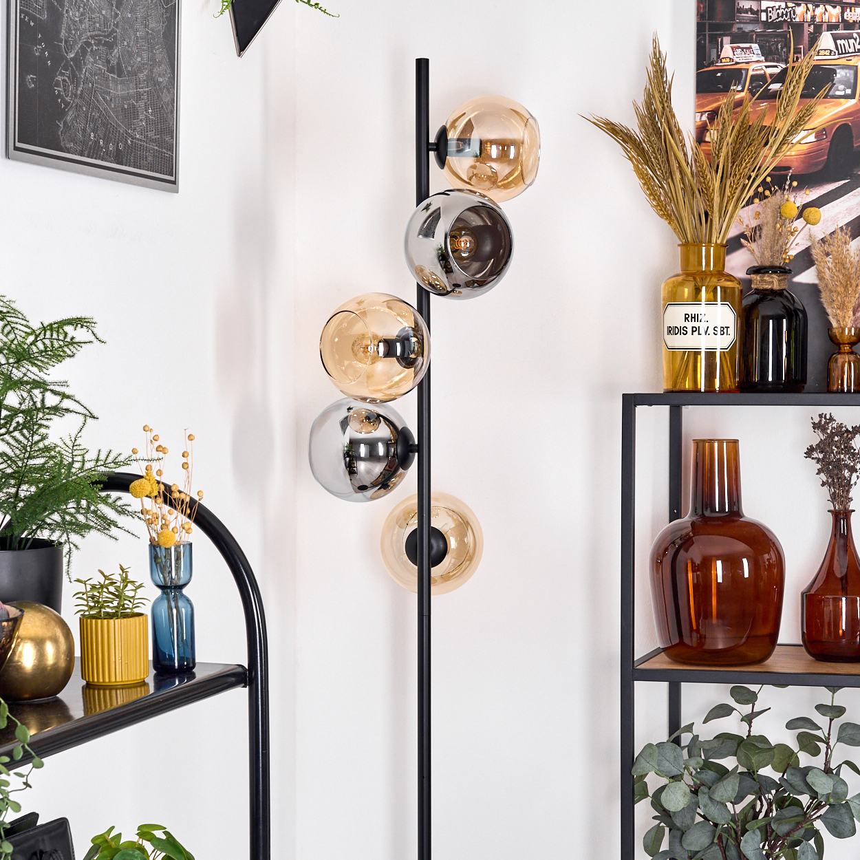 Eine moderne Stehlampe mit Glaskugeln, schwarzem Metallrahmen und verschiedenen Dekorationsartikeln auf Regalen.