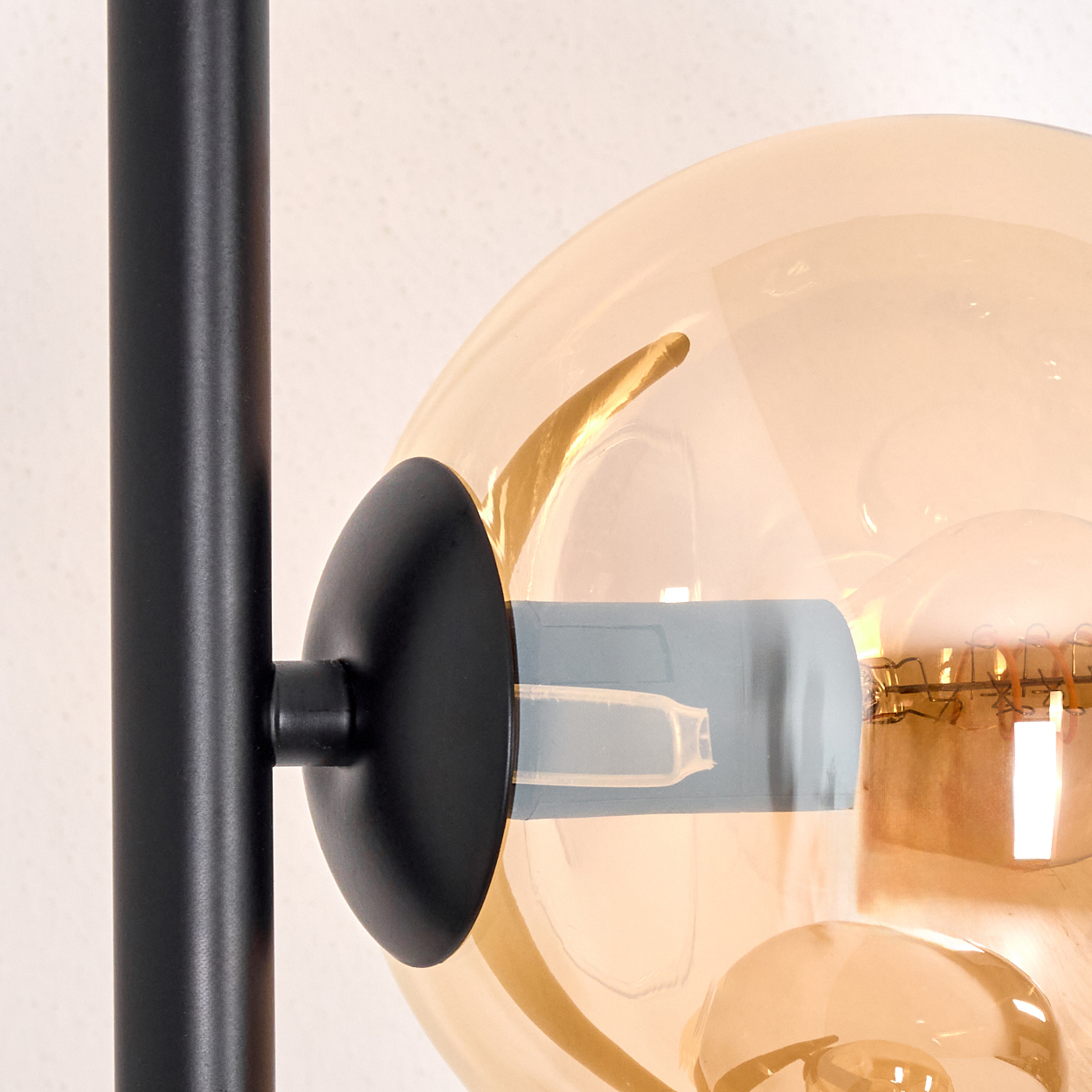 Nahaufnahme einer modernen Lampe. Sie hat eine schwarze Stange und einen runden, transparenten, bernsteinfarbenen Glasschirm.