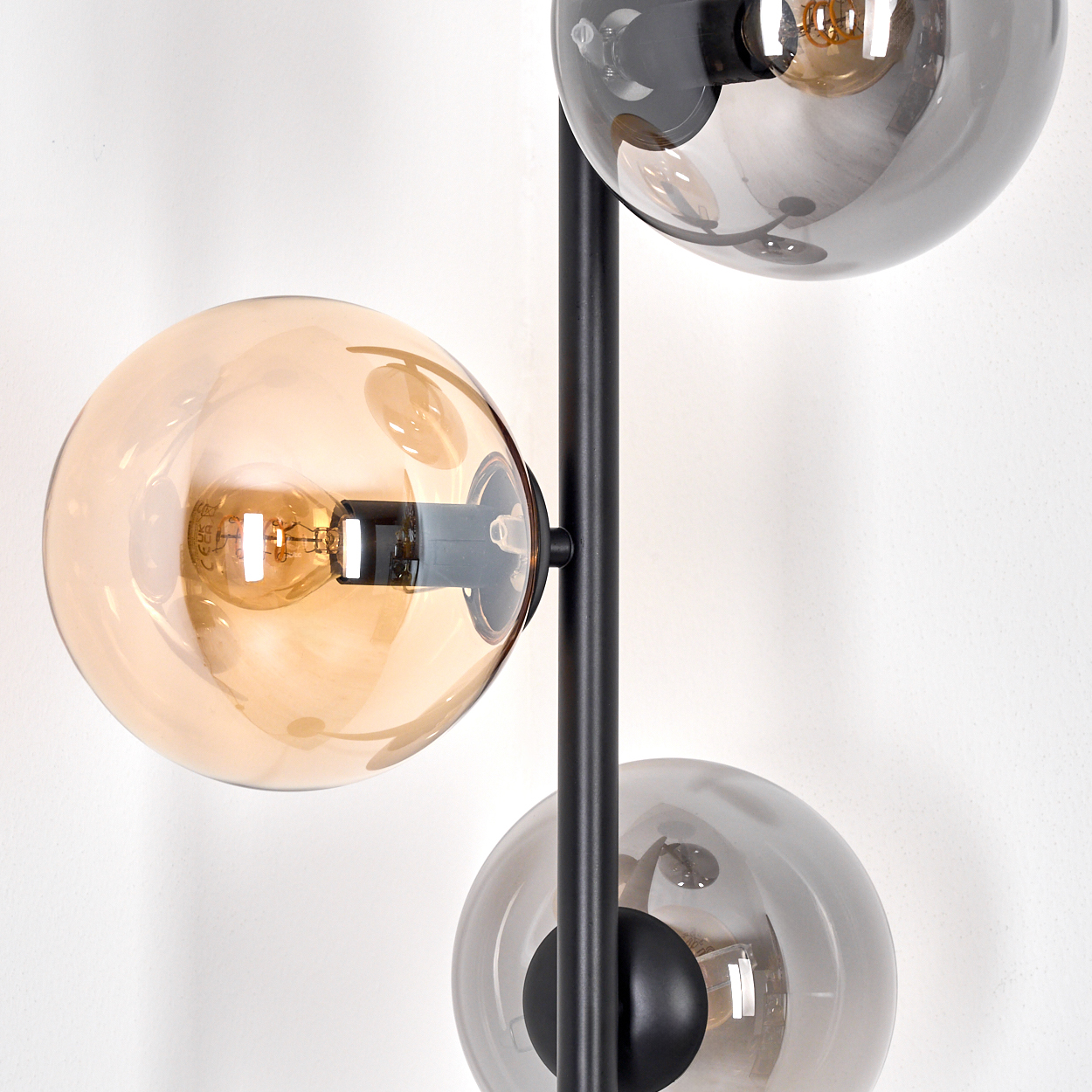 Eine moderne Lampe mit drei kugelförmigen Schirmen. Die Schirme sind bernsteinfarben und grau, mit schwarzem Metall auf weißer Wand.