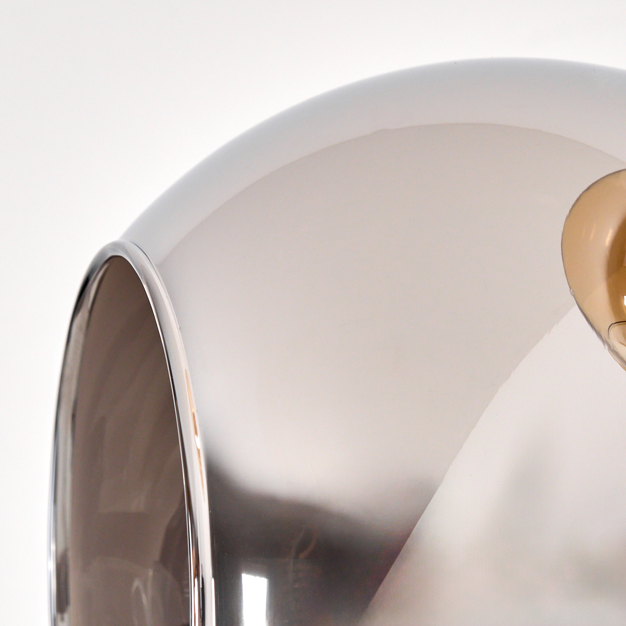 Nahaufnahme einer metallischen Lampe mit geschwungenem Design. Rechts ist eine braune Glühbirne zu sehen. Der Hintergrund ist weiß.