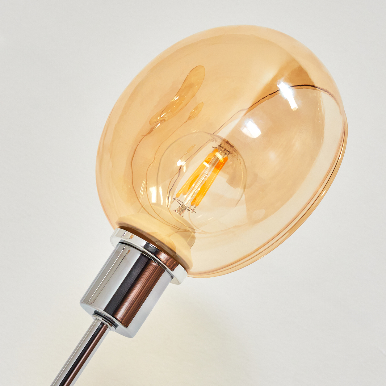 Nahaufnahme einer Glühbirne. Die Glühbirne hat eine warme orange Farbe und ist in einem klaren Glas eingeschlossen. Der Sockel ist silberfarben und der Hintergrund ist weiß.