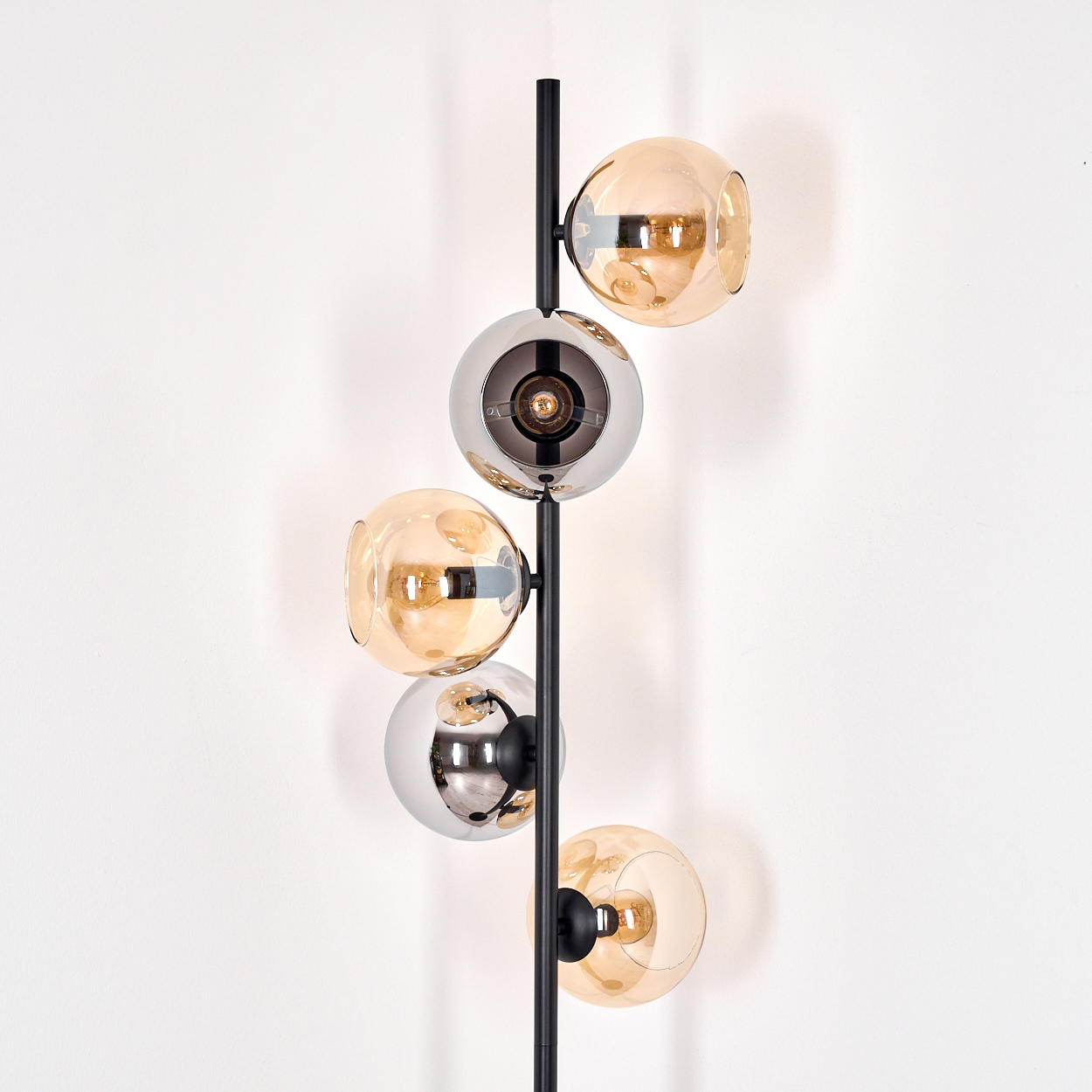 Eine moderne Stehlampe mit fünf kugelförmigen Glasschirmen, die sich zwischen Bernstein und verspiegeltem Silber abwechseln, auf einem schwarzen Pfahl.