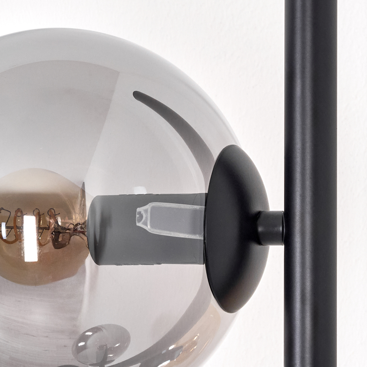 Nahaufnahme einer Lampe. Eine klare Kugel umgibt eine Glühbirne, die an einer schwarzen Metallstange und -halterung befestigt ist.