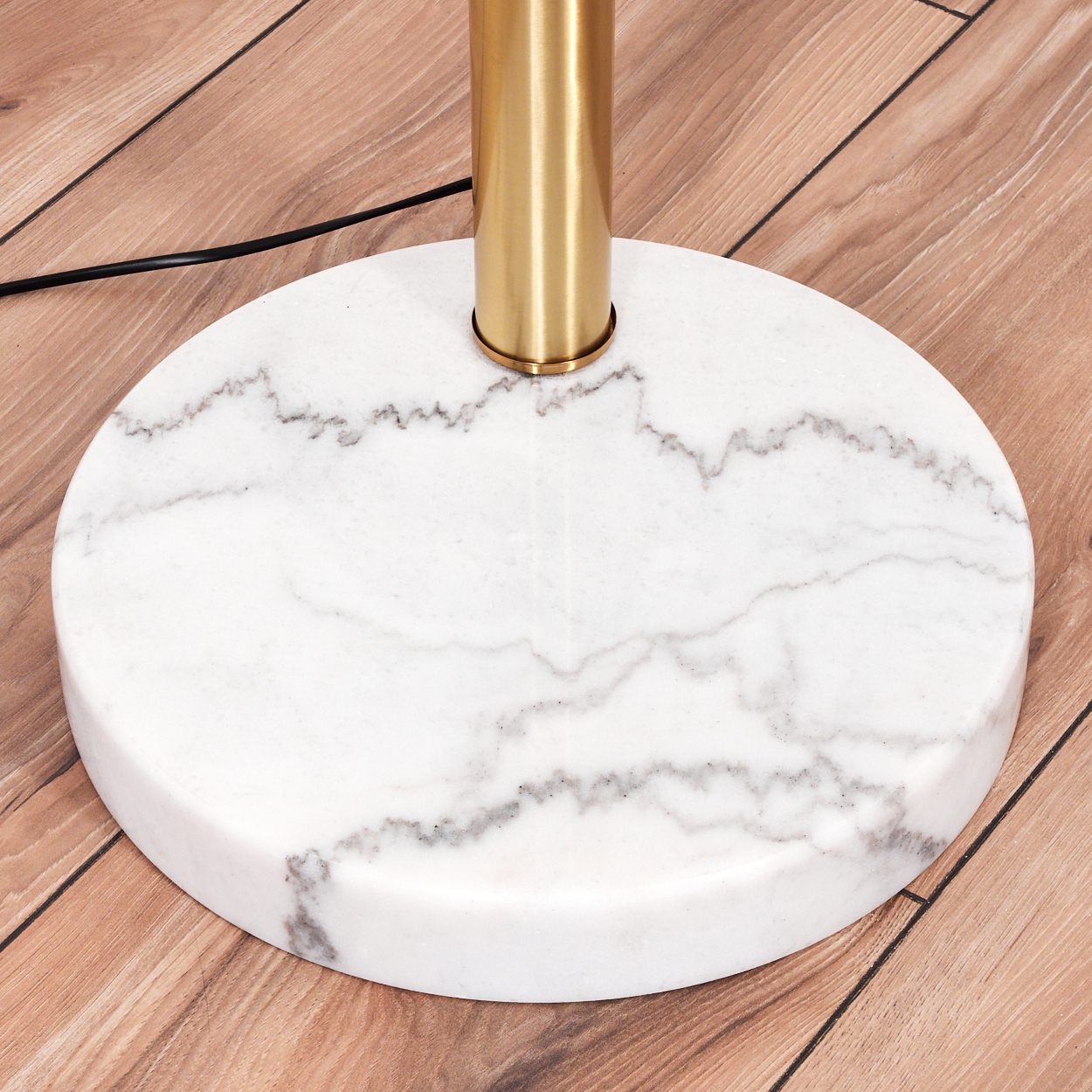 Nahaufnahme eines Lampenfußes. Er hat einen Sockel aus weißem Marmor mit grauer Maserung, eine goldene Stange und einen Holzboden.