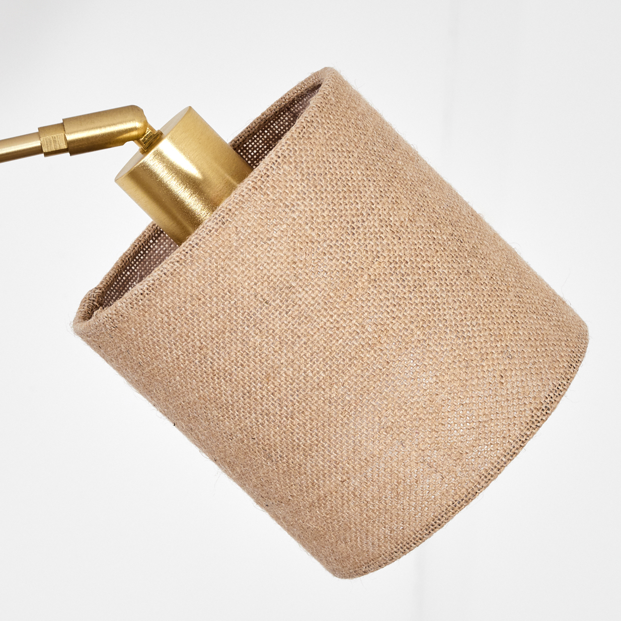 Nahaufnahme einer Lampe mit beigem Lampenschirm und goldenen Metallkomponenten auf weißem Hintergrund.