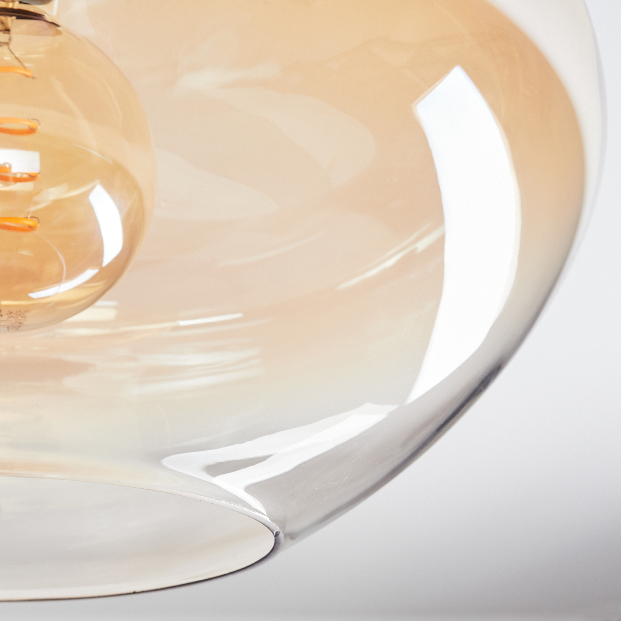 Nahaufnahme einer Glasleuchte mit einer warm getönten Glühbirne. Das Glas ist klar und gebogen, mit einem weichen, bernsteinfarbenen Farbverlauf.