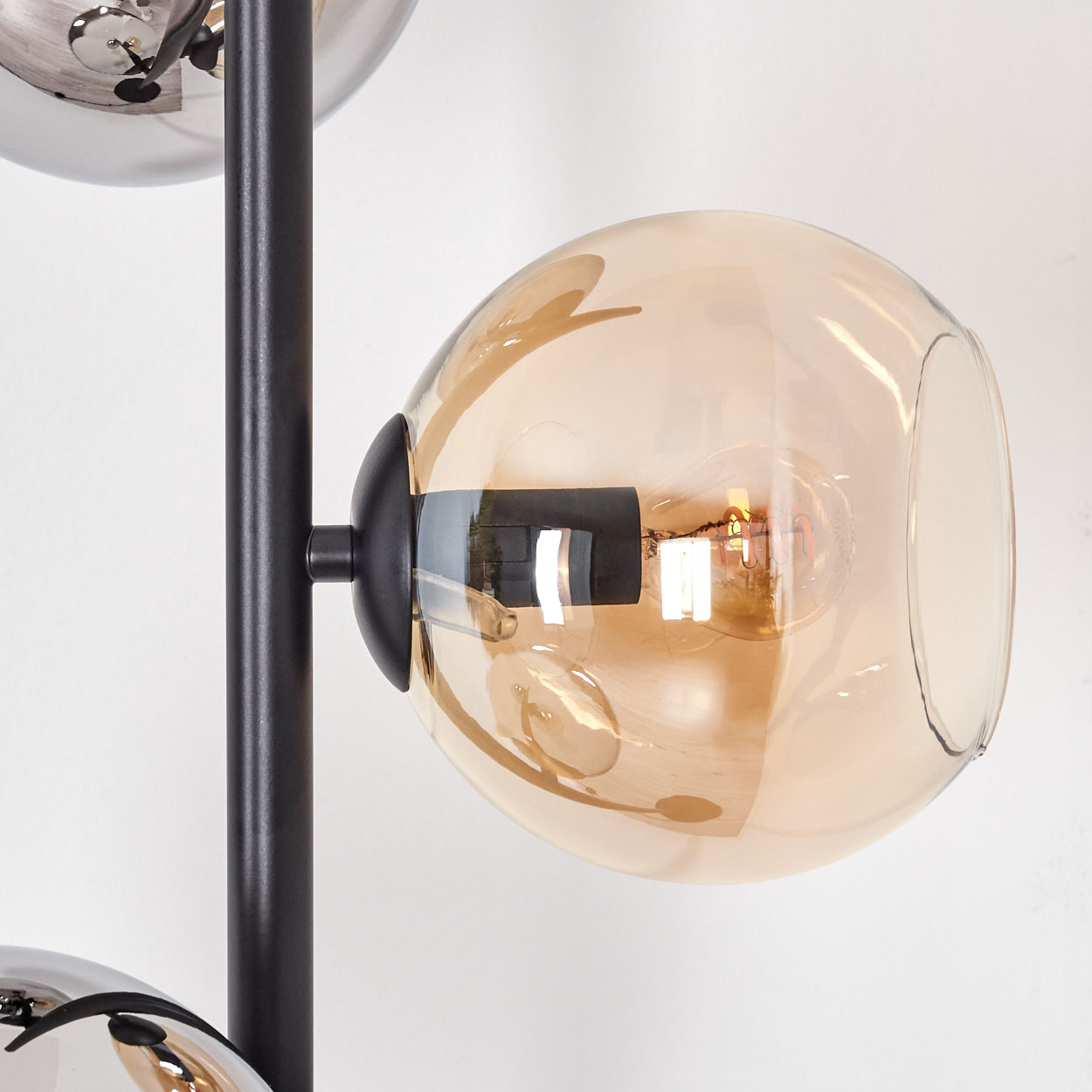 Eine moderne Lampe mit schwarzem Rahmen und mehreren Glaskugeln, eine bernsteinfarben mit sichtbarer Glühbirne.