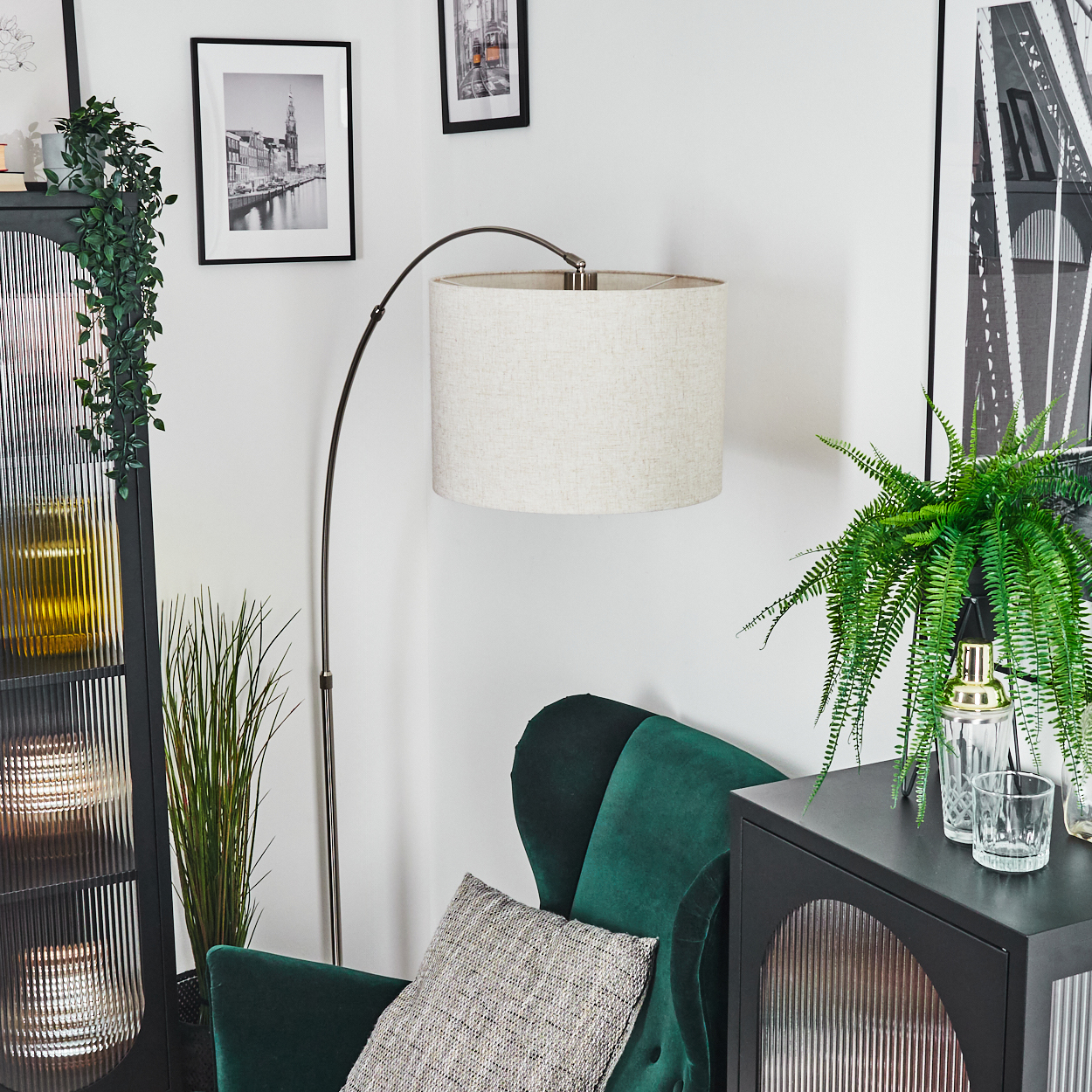 Eine Zimmerecke mit grünem Stuhl, Lampe und Schrank. Bilder hängen an der Wand. Pflanzen und Gläser stehen auf dem Schrank.