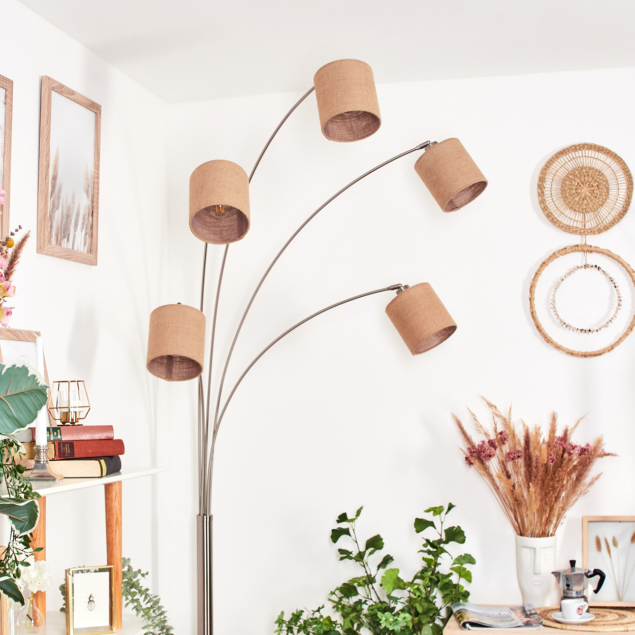 Eine moderne Stehlampe mit fünf Lampenschirmen. Eine Vase mit Trockenblumen, Bildern und Pflanzen sind sichtbar.