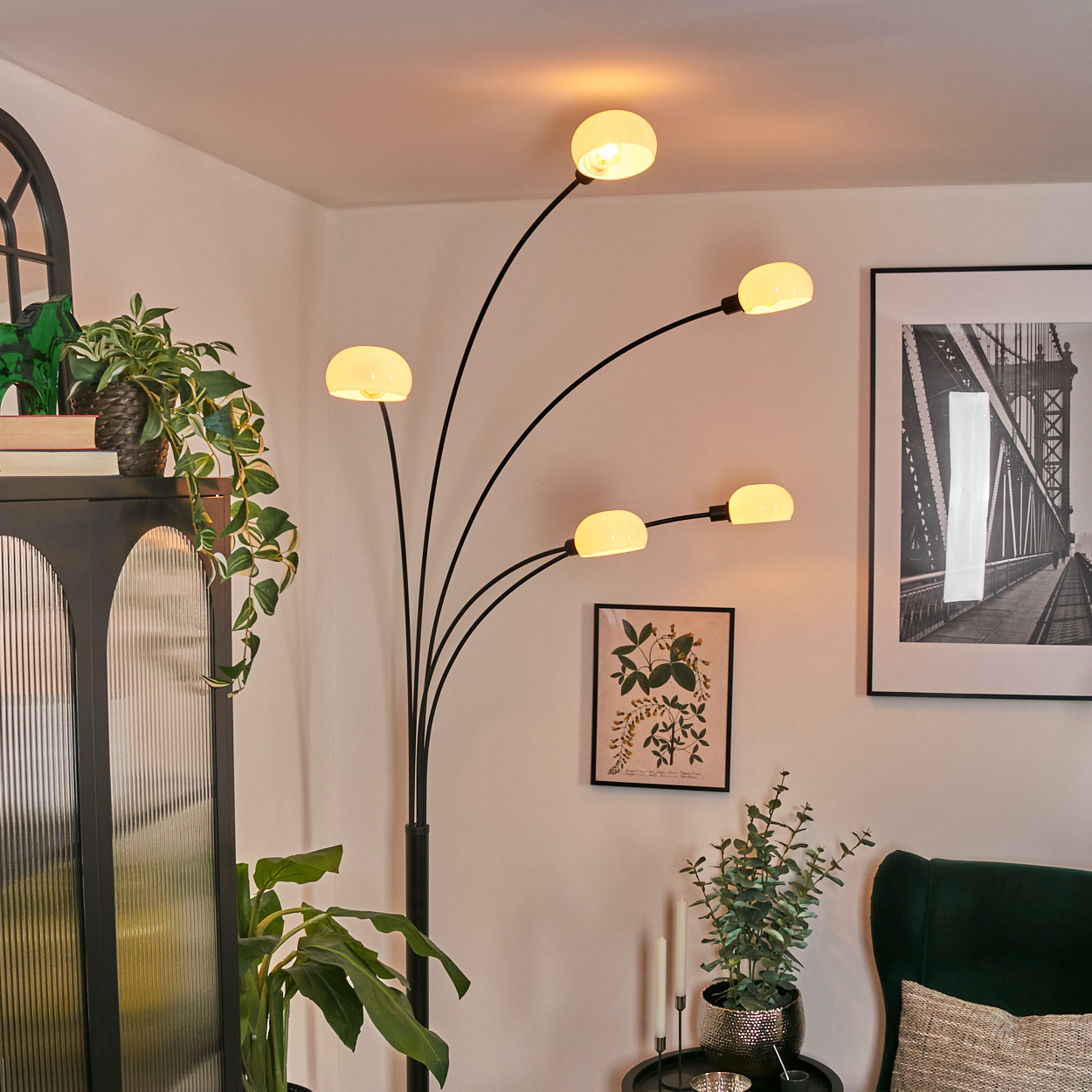 Ein modernes Wohnzimmer mit einer mehrköpfigen Stehlampe, Kunstwerken, Pflanzen und einem dunkelgrünen Sessel.
