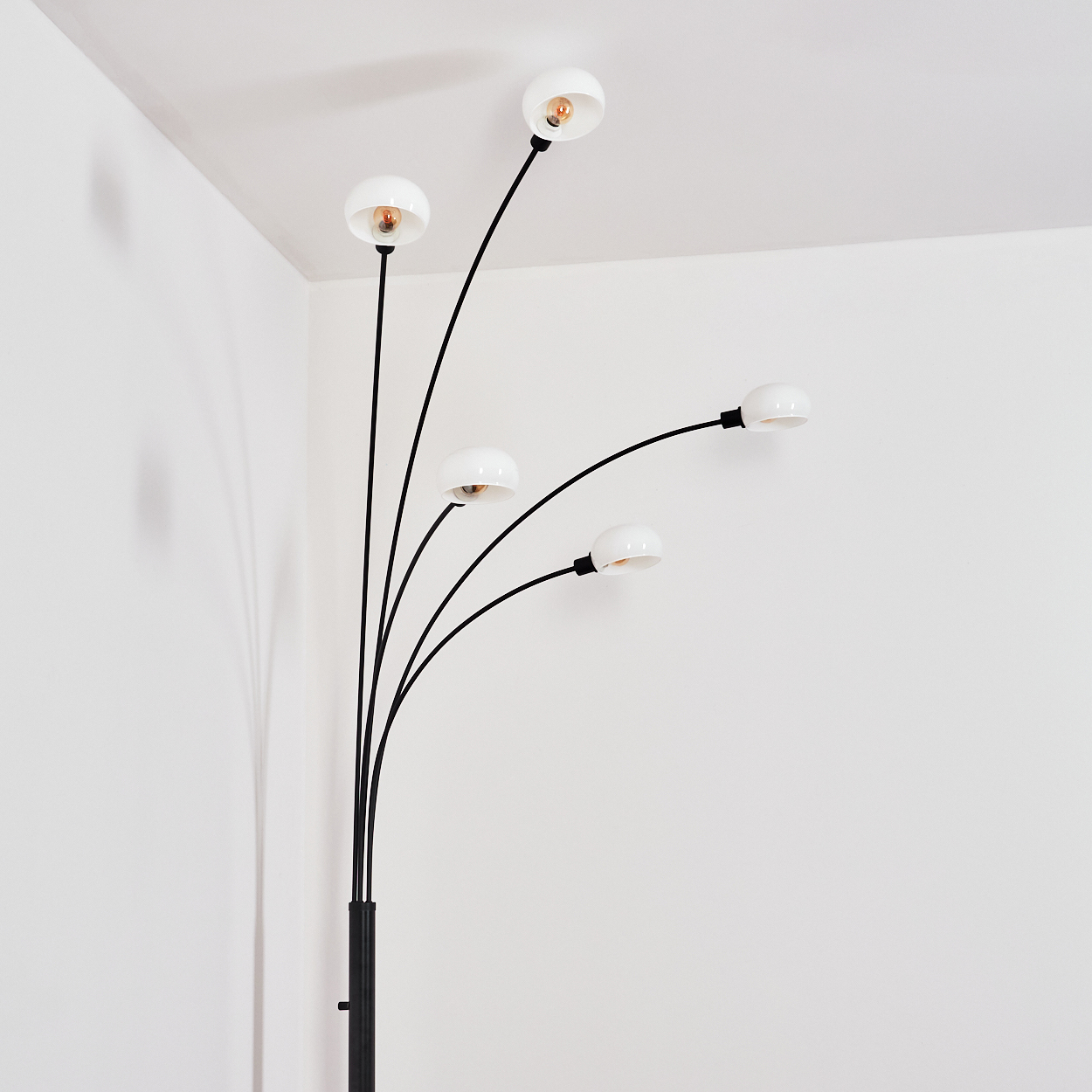 Eine moderne Stehlampe mit fünf weißen Lampenschirmen und schwarzen Stielen vor einer weißen Wand. Die Lampenschirme haben Glühbirnen.