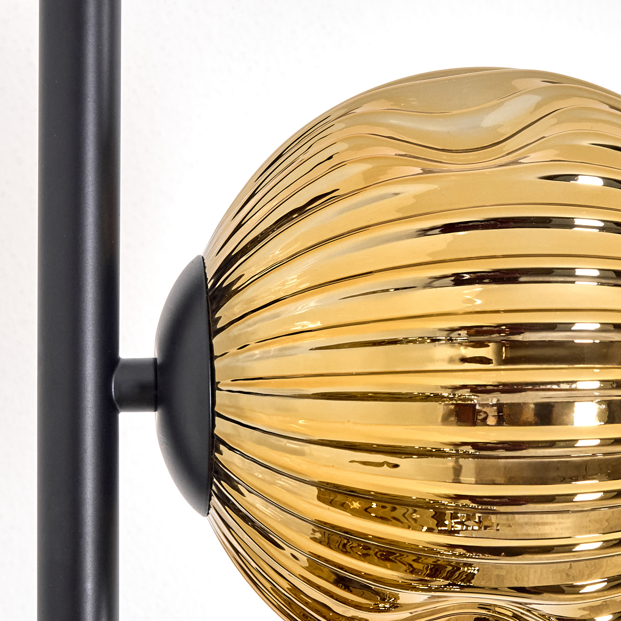 Nahaufnahme einer goldenen, gerippten Glaskugel, die an einer schwarzen Metallsäule befestigt ist. Der Hintergrund ist weiß.