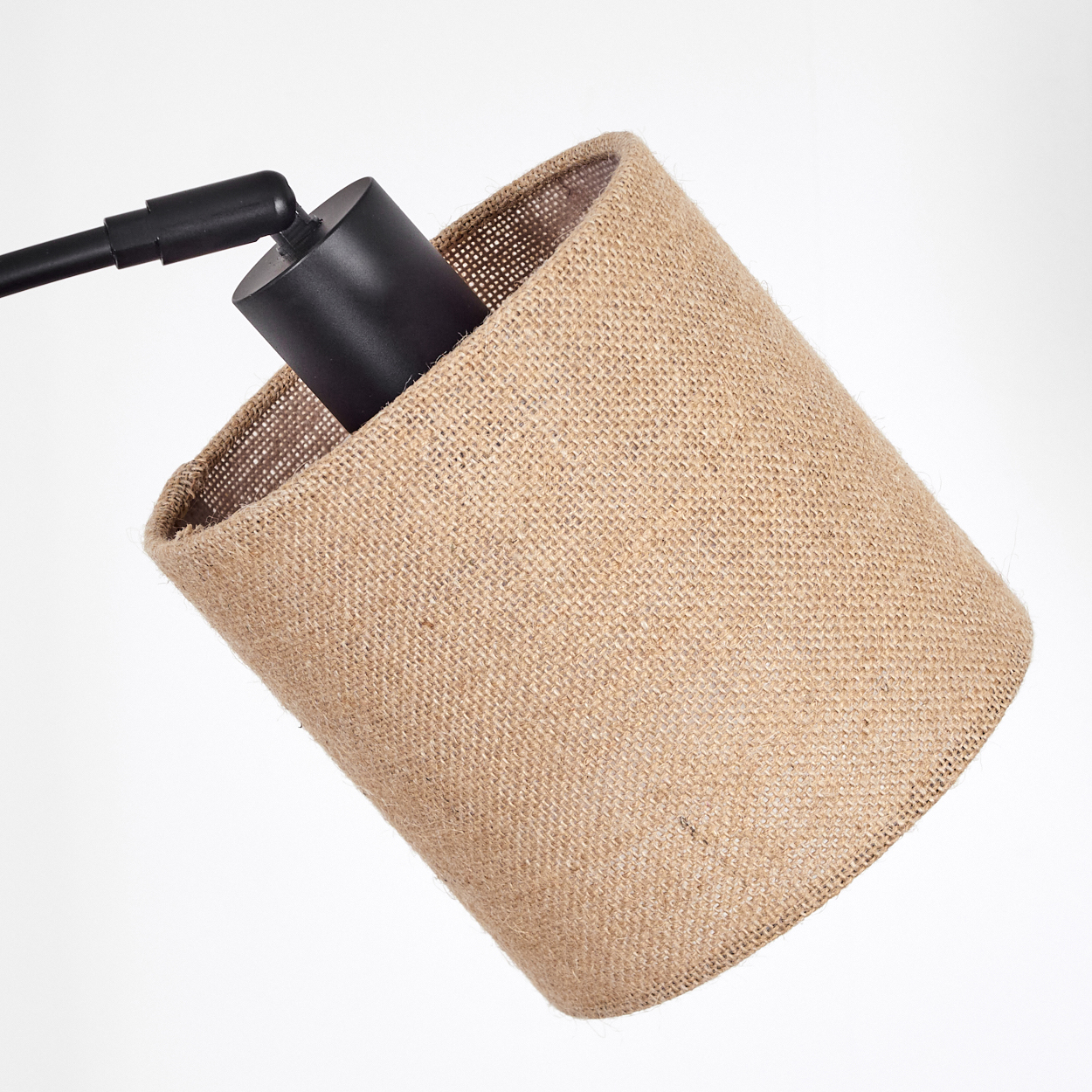 Nahaufnahme eines Lampenschirms aus Jute. Der Schirm ist braun und steht vor einem weißen Hintergrund. Die Lampe ist schwarz.